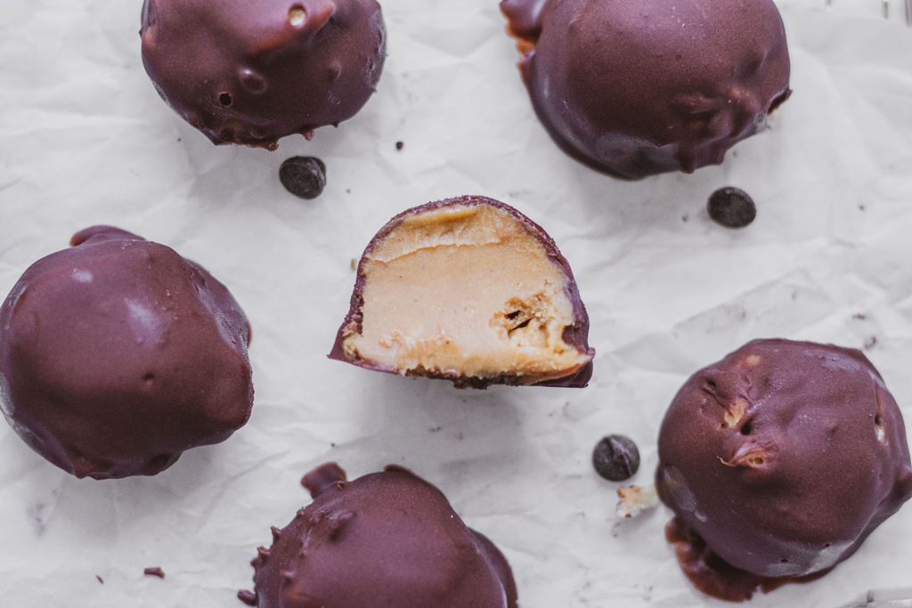 Keto Chocolate Peanut Butter Fat Bombs. Chocolate covered peanut butter balls on a white surface and wore wrack.