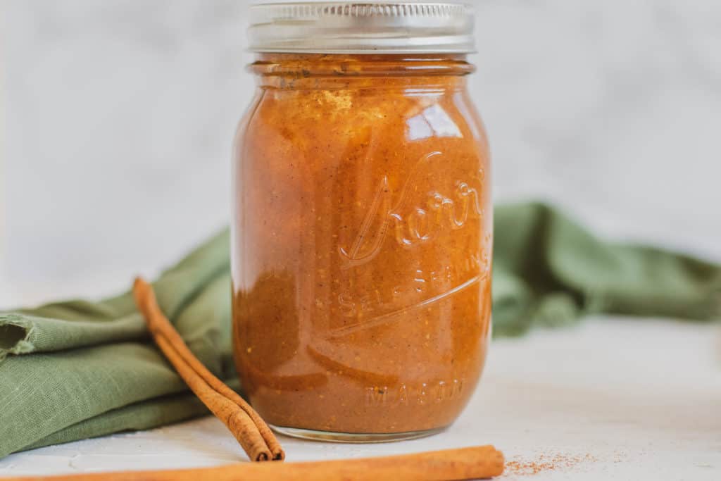 Low carb Pumpkin Spice Syrup in a glass jar, with cinnamon sticks on the side and a green napkin in the back.