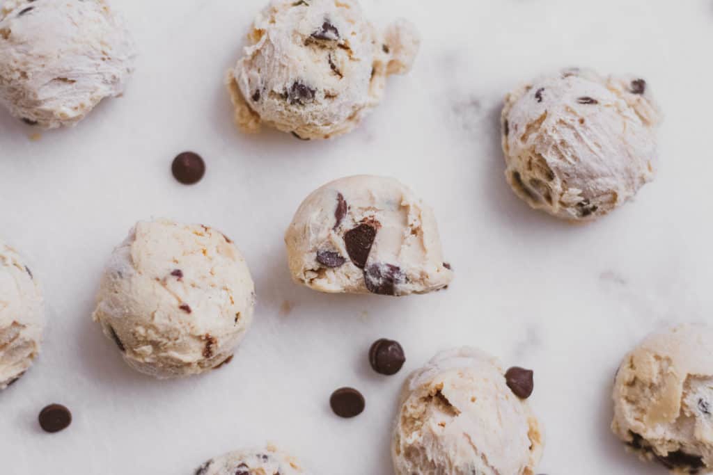Low carb keto cookie dough fat bombs on a white surface with chocolate chips scattered around.