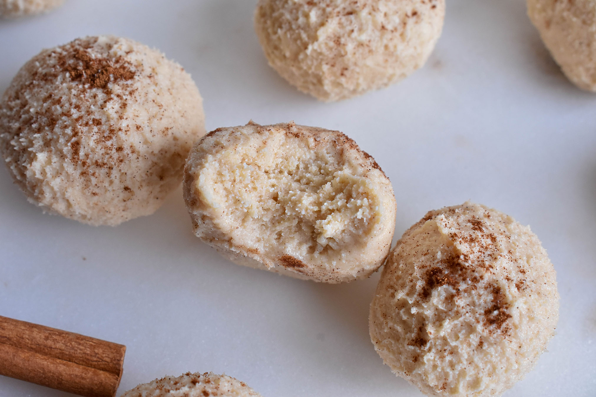 Light brown fat bombs in the shape of balls with cinnamon sprinkled on top on top of a white table top.