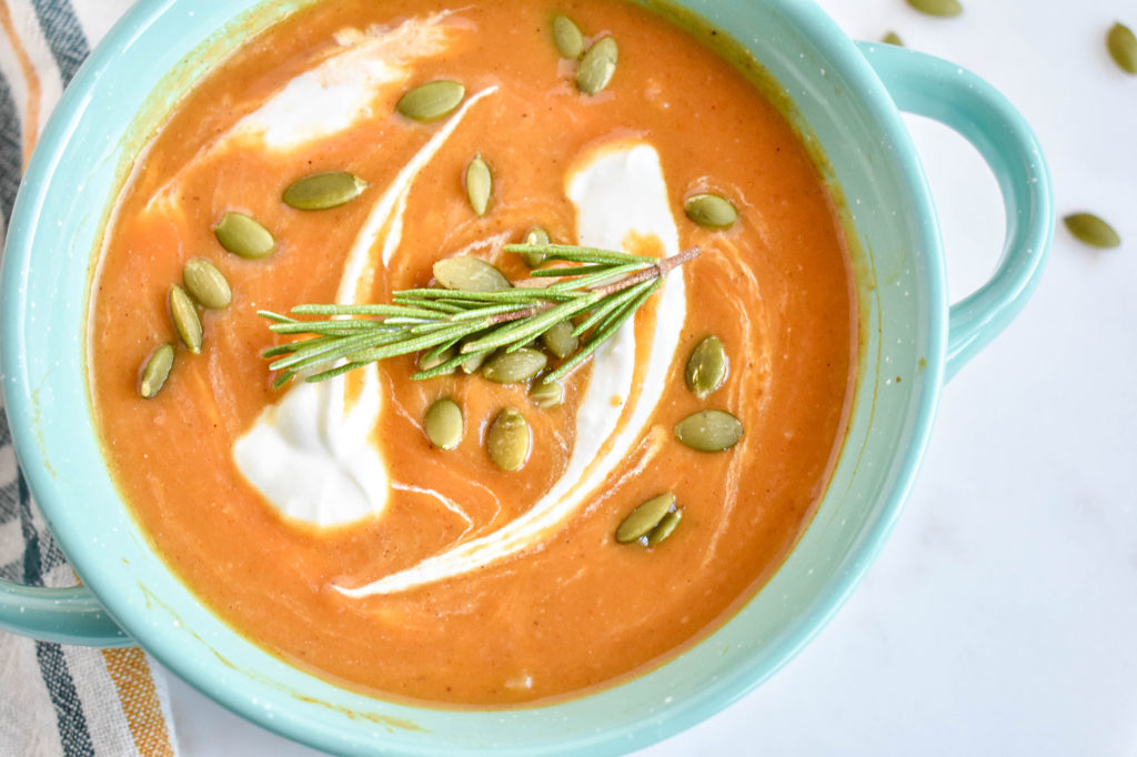 Low carb savory pumpkin soup in a blue bowl with cream swirled in and rosemary on top.