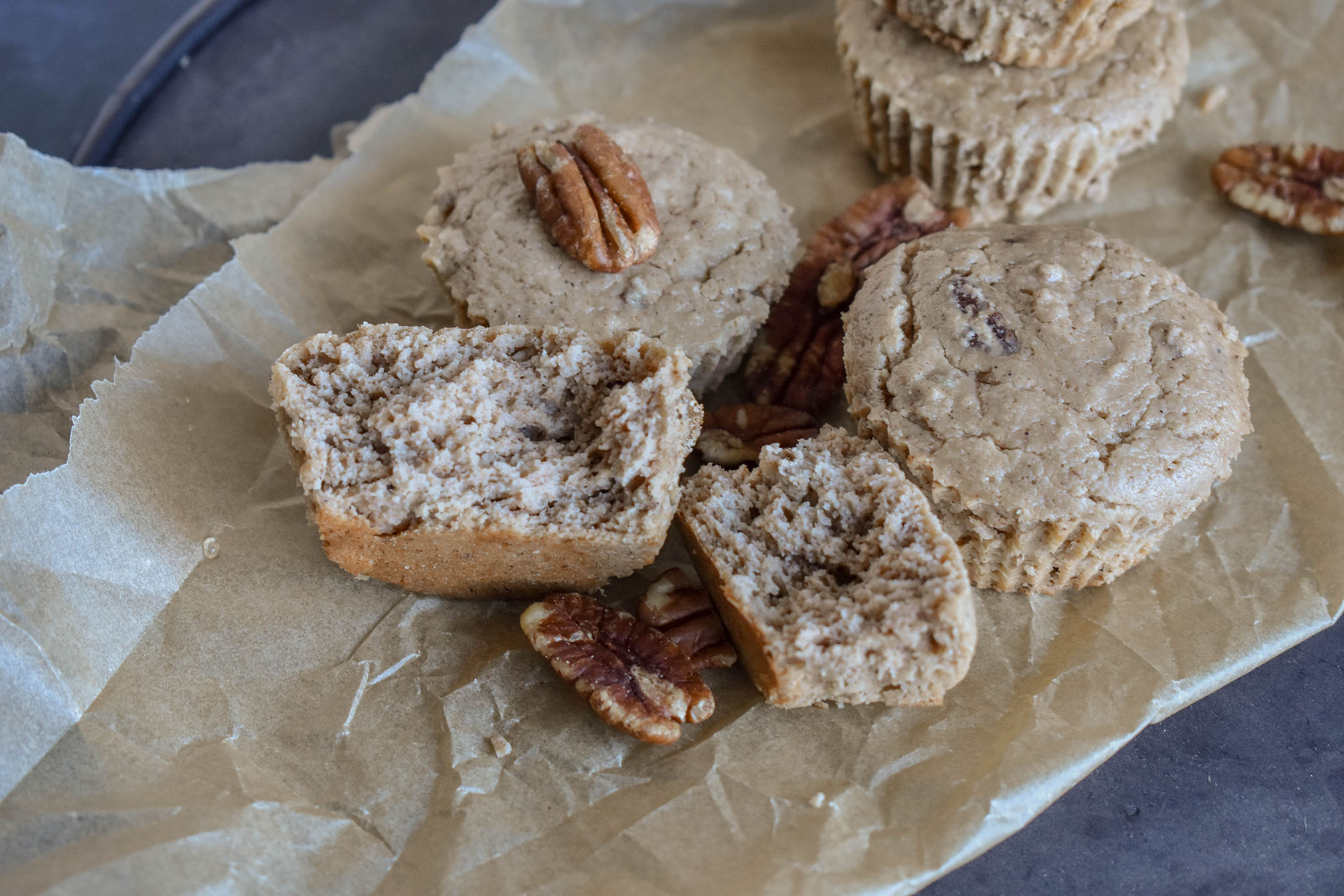 Light brown muffins laying on parchment paper with pecans laid on top.