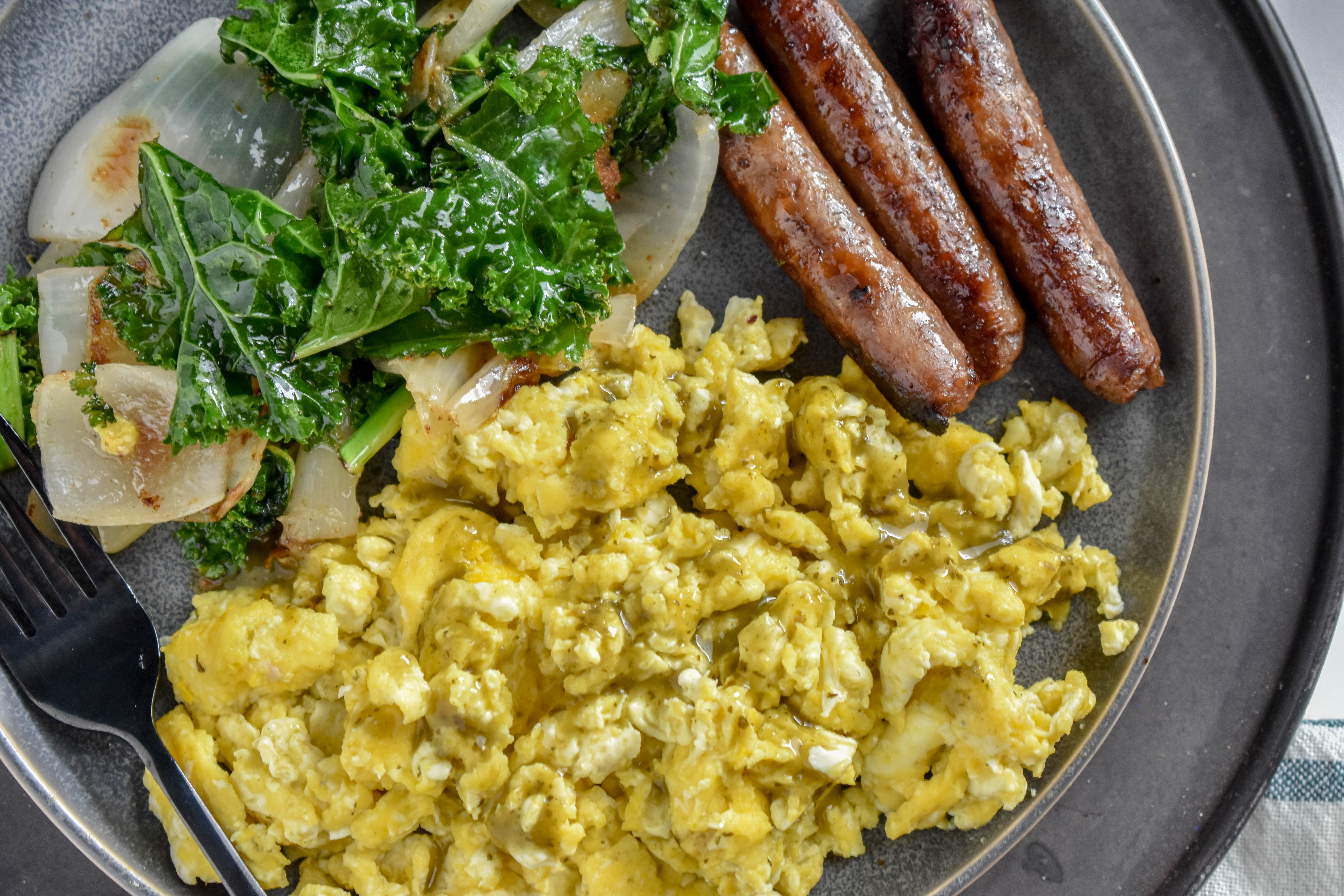Clean Eating Breakfast with scrambled eggs, sausage links and sauteed kale and onions on a grey plate.