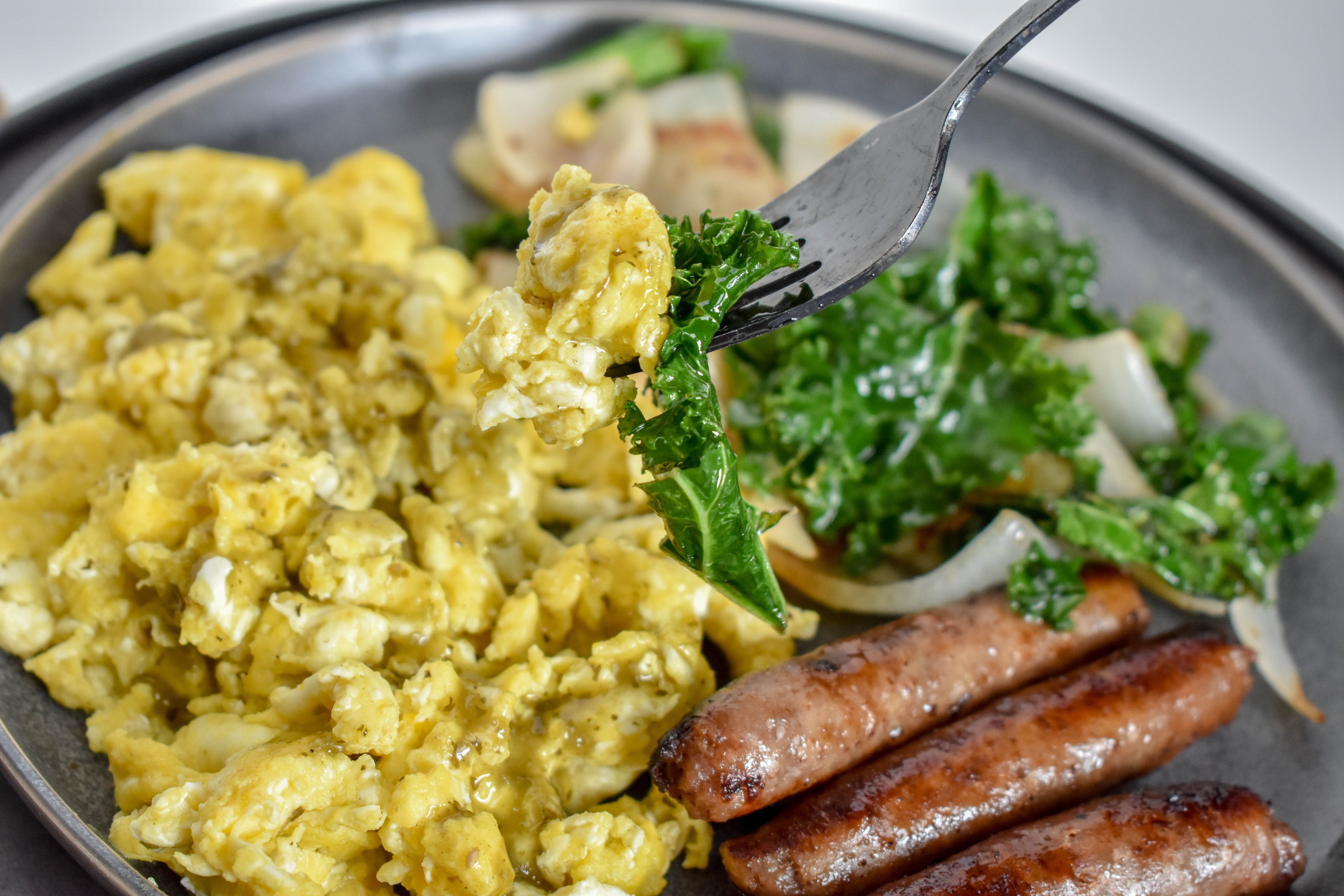 Clean Eating Breakfast with scrambled eggs, sausage links and sauteed kale and onions on a grey plate.
