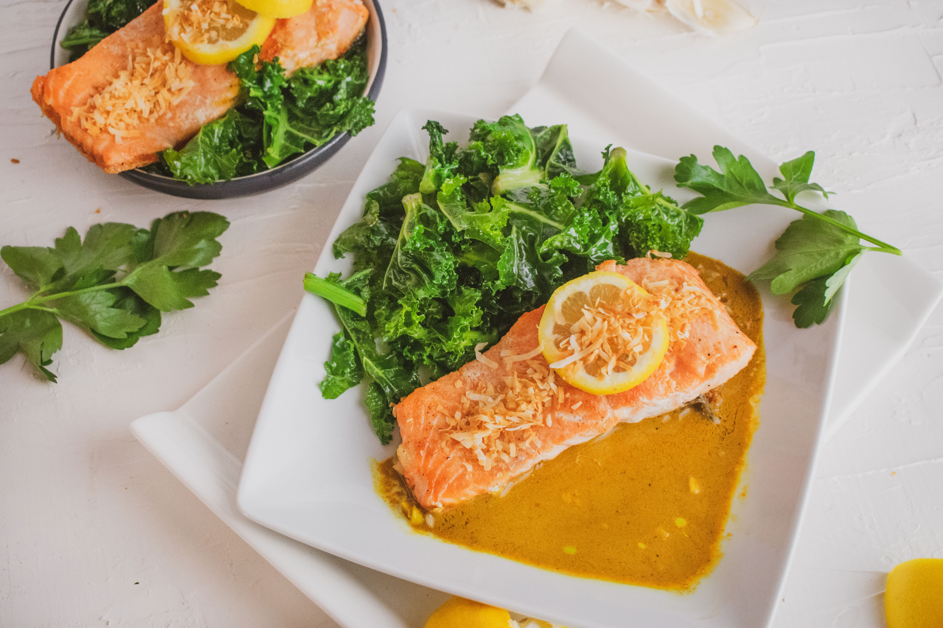 Salmon filet in curry and and kale salad on the side on a white surface 