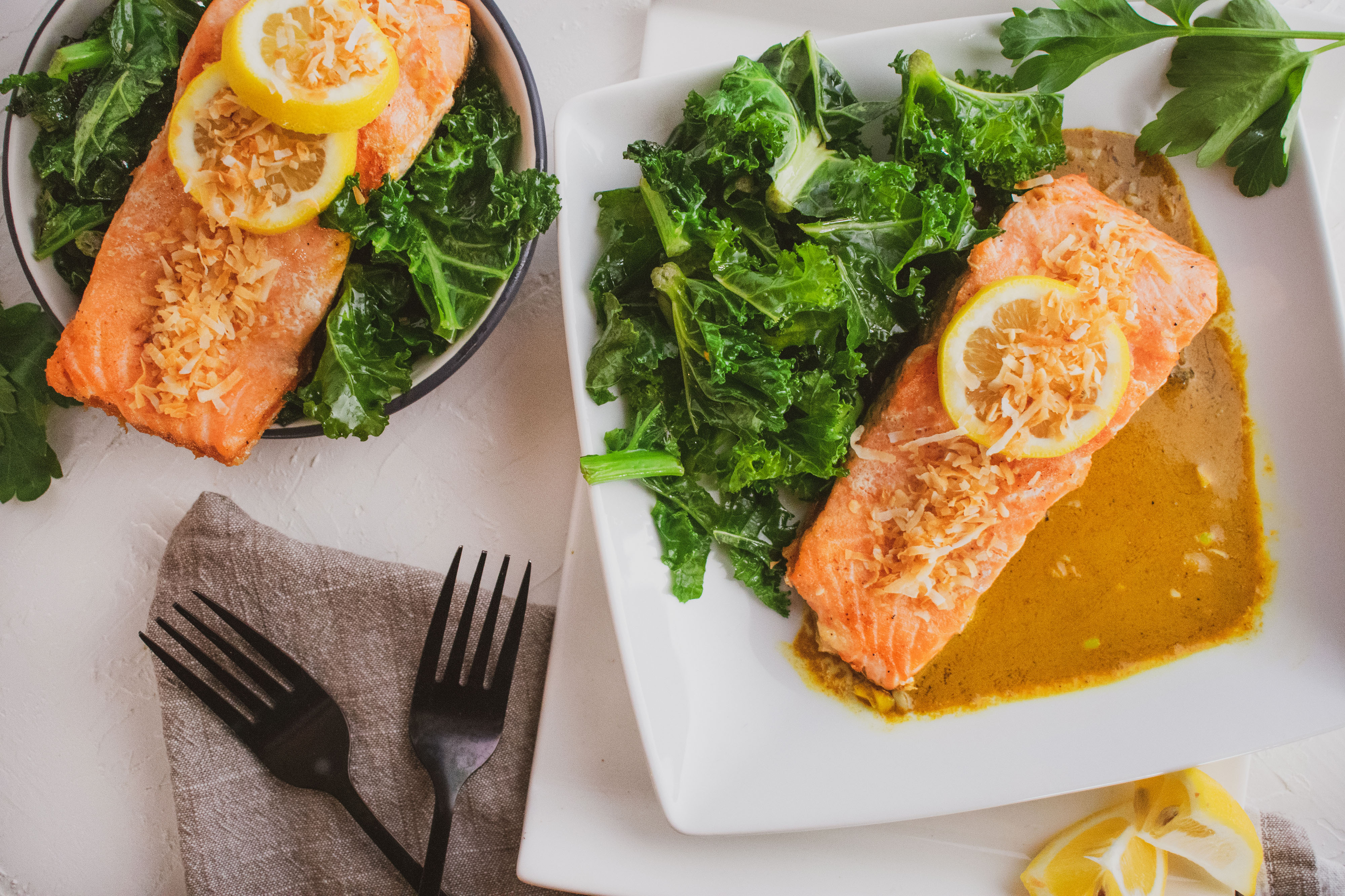 Salmon filet in curry and and kale salad on the side on a white surface 