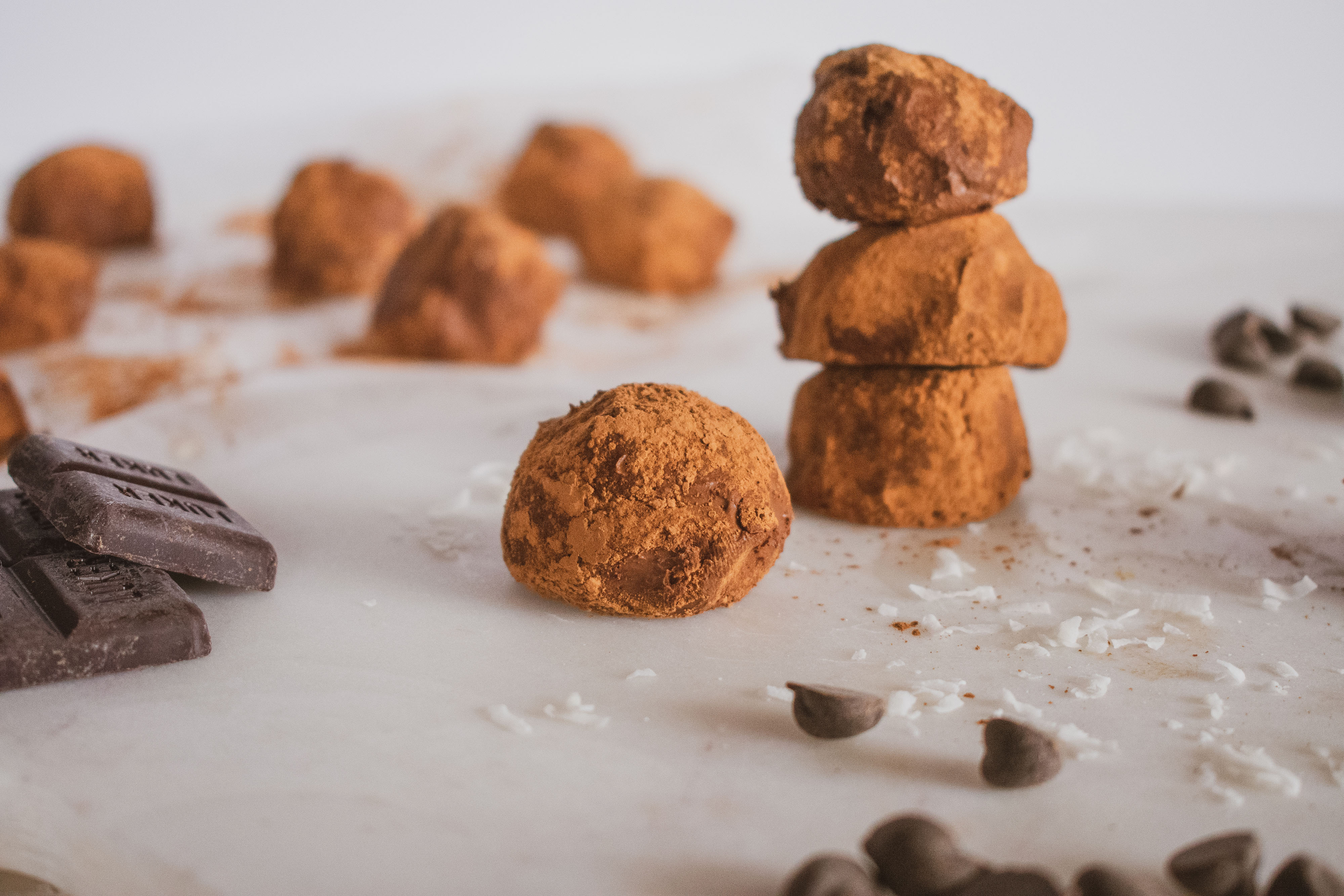 Cocoa powder covered keto chocolate truffles. Set on a white surface with chocolate chips.