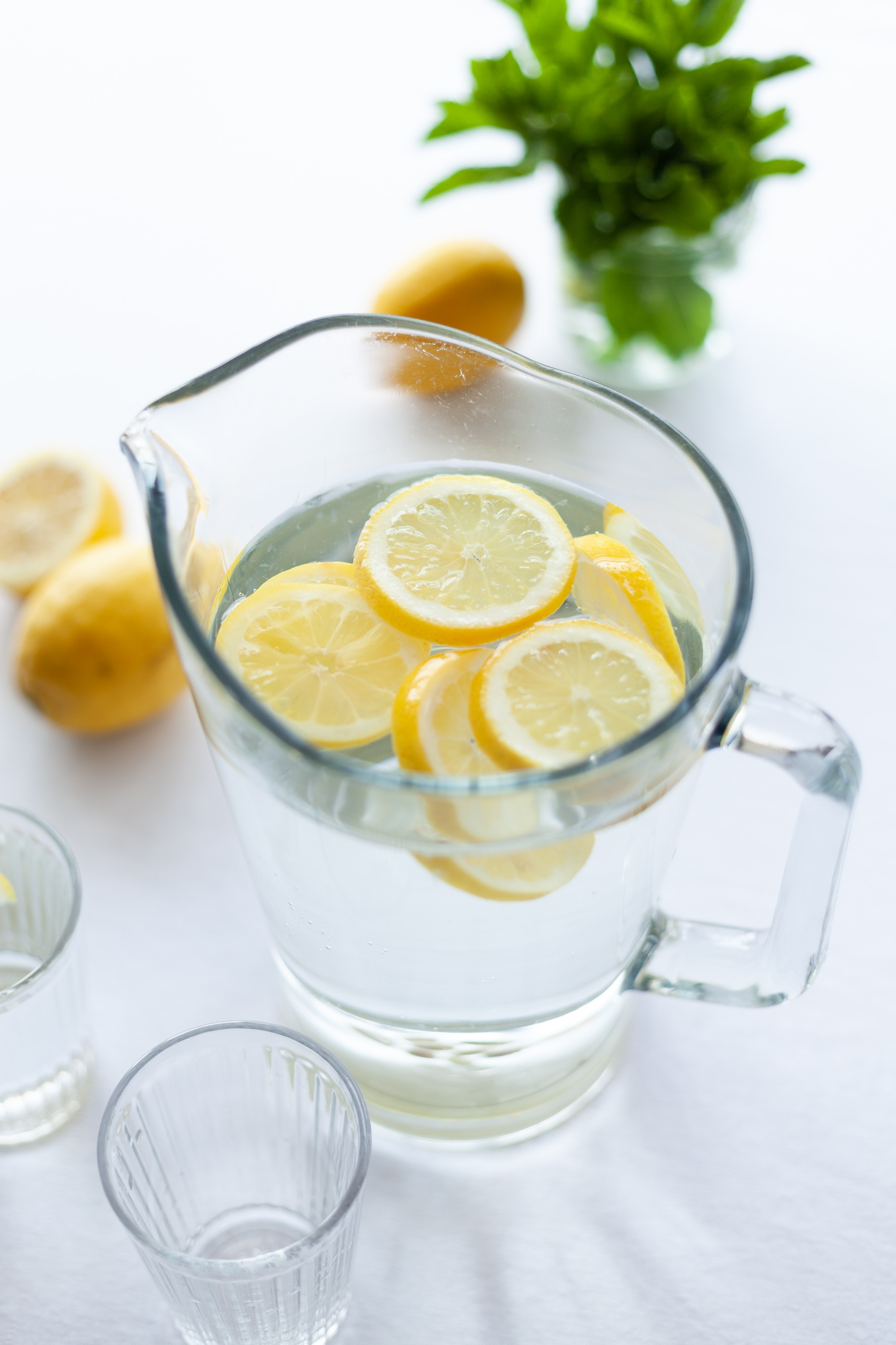 Lemons floating in a pitcher of water with lemons and greens in the background