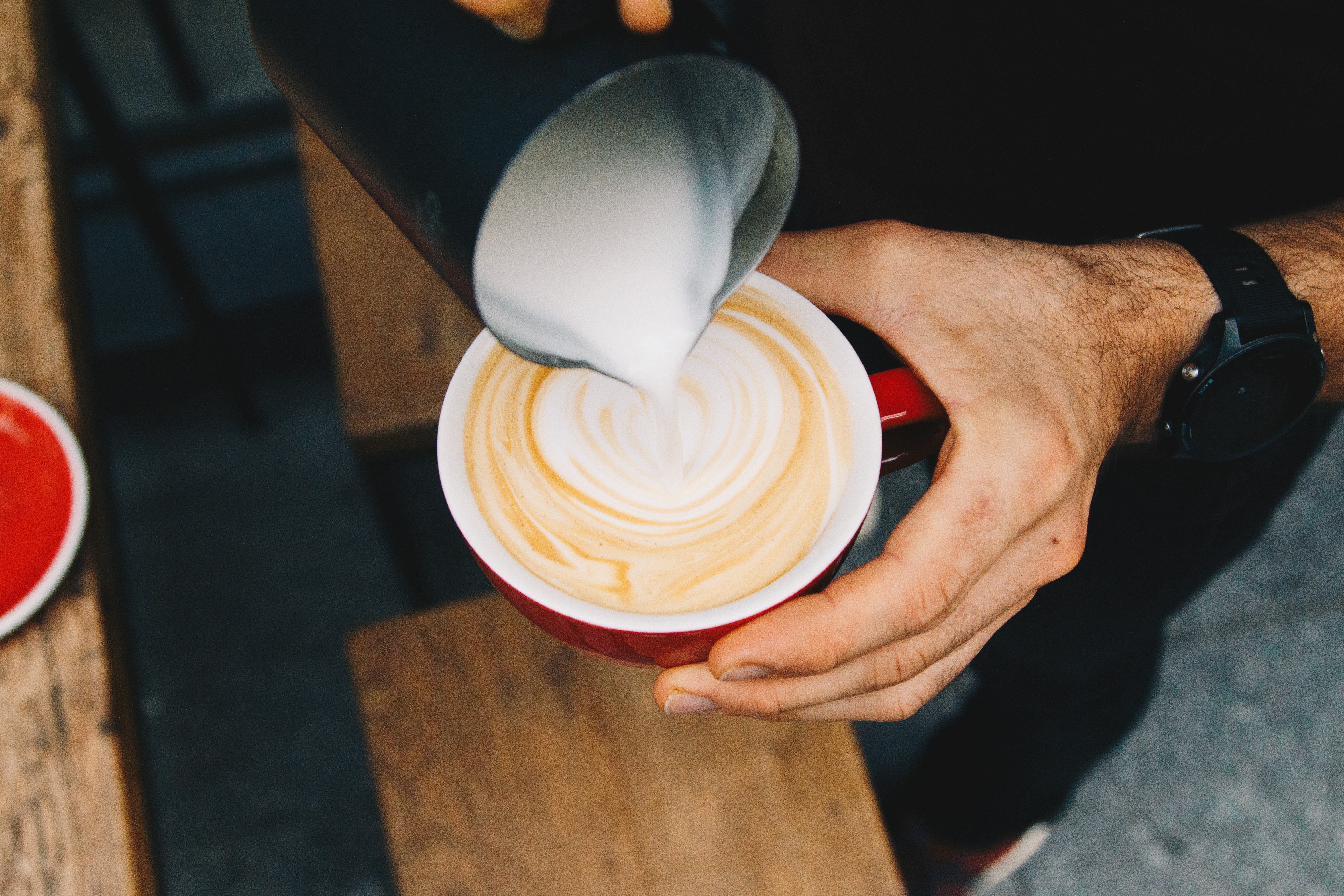 Milk pouring into a cup of coffee with man hands holding it.