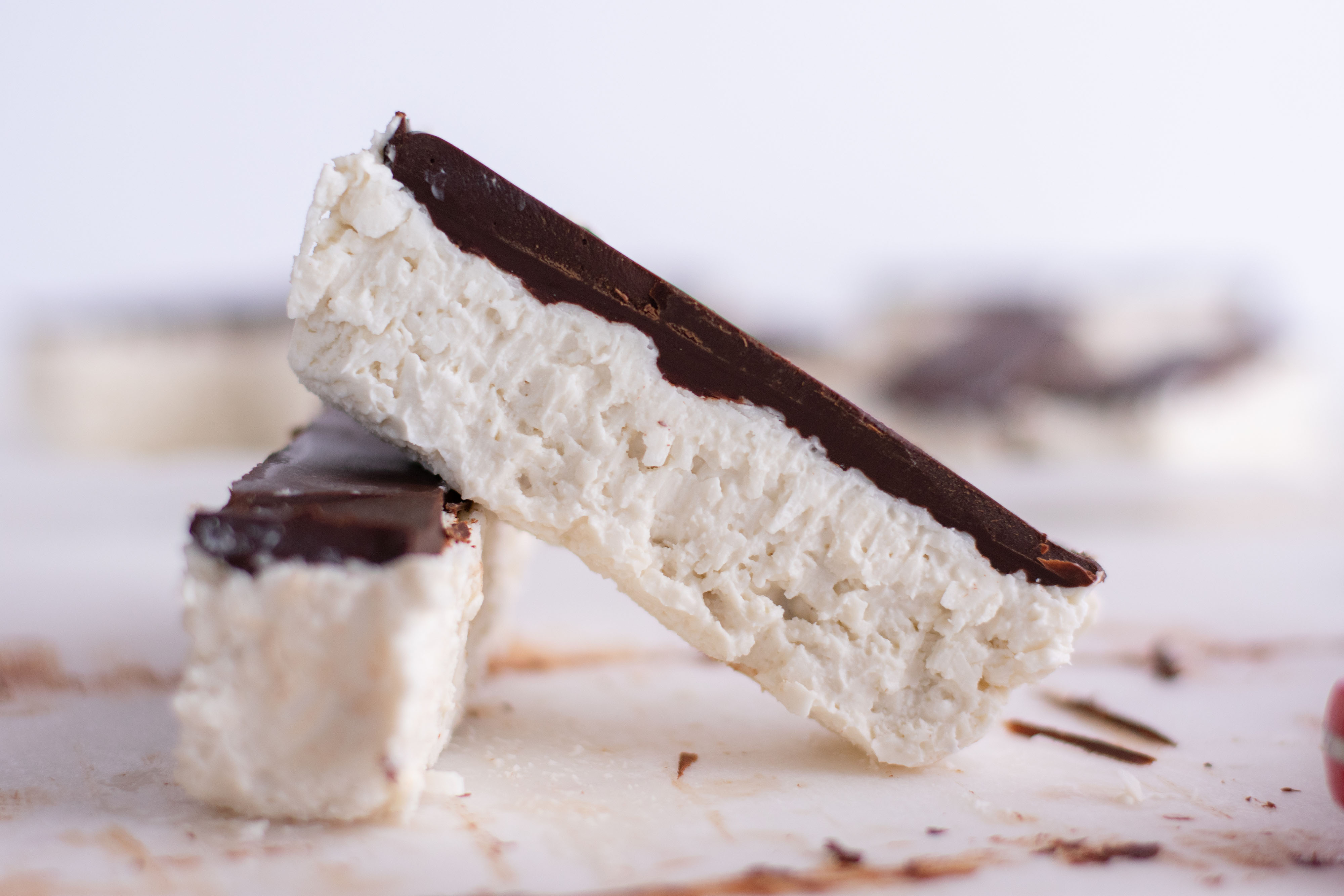 White coconut bars with a chocolate layer on top. laid out on a white surface
