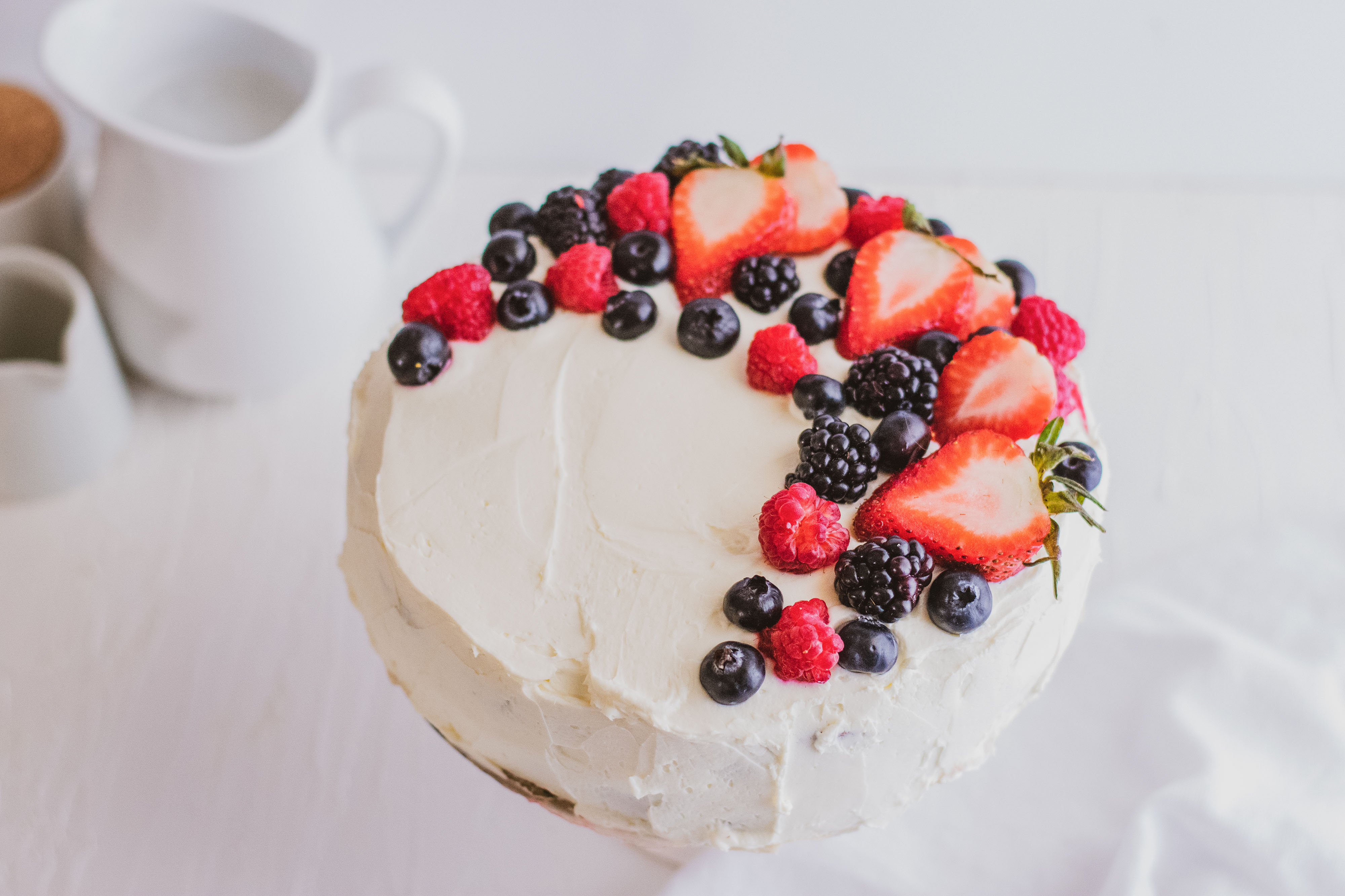 Keto Chantilly Cake a white cake with berries covering the top on a cake stand with a white background