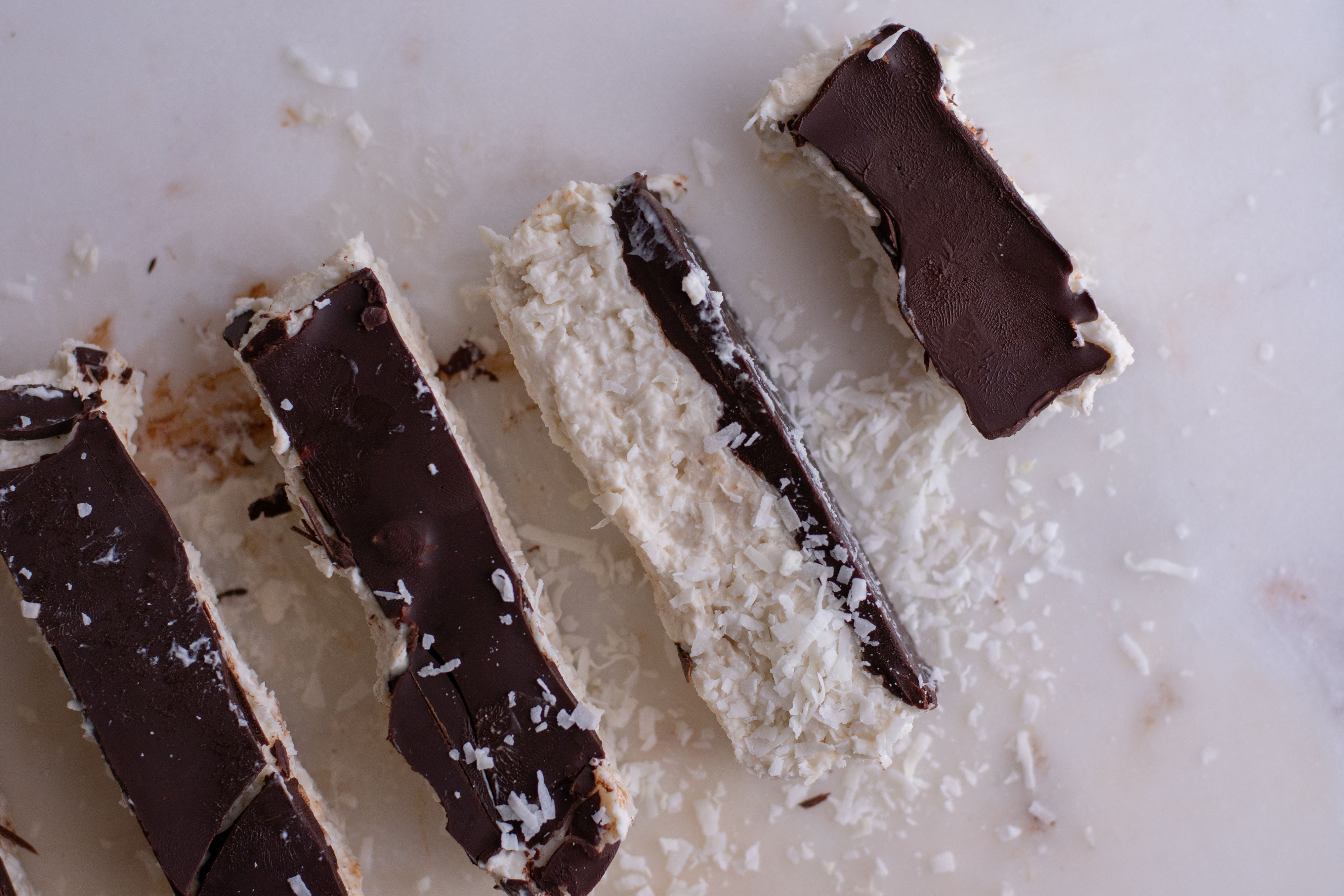 White coconut bars with a chocolate layer on top. laid out on a white surface
