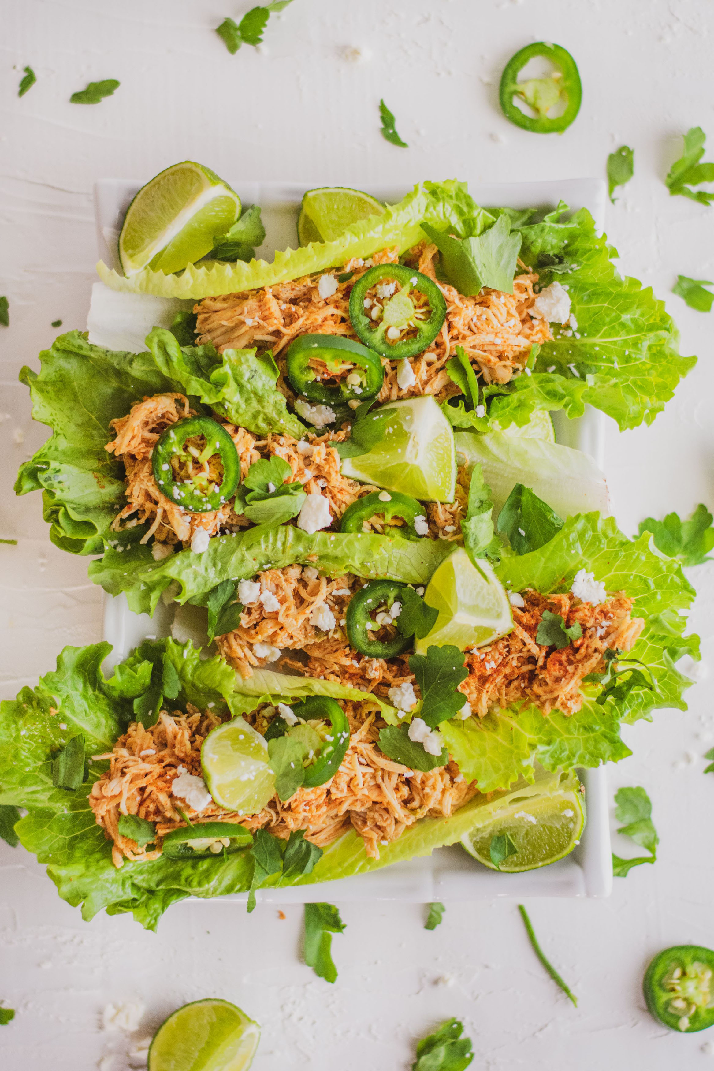 Shredded chicken tacos in lettuce wraps with fetta cheese, limes and jalapenos on top