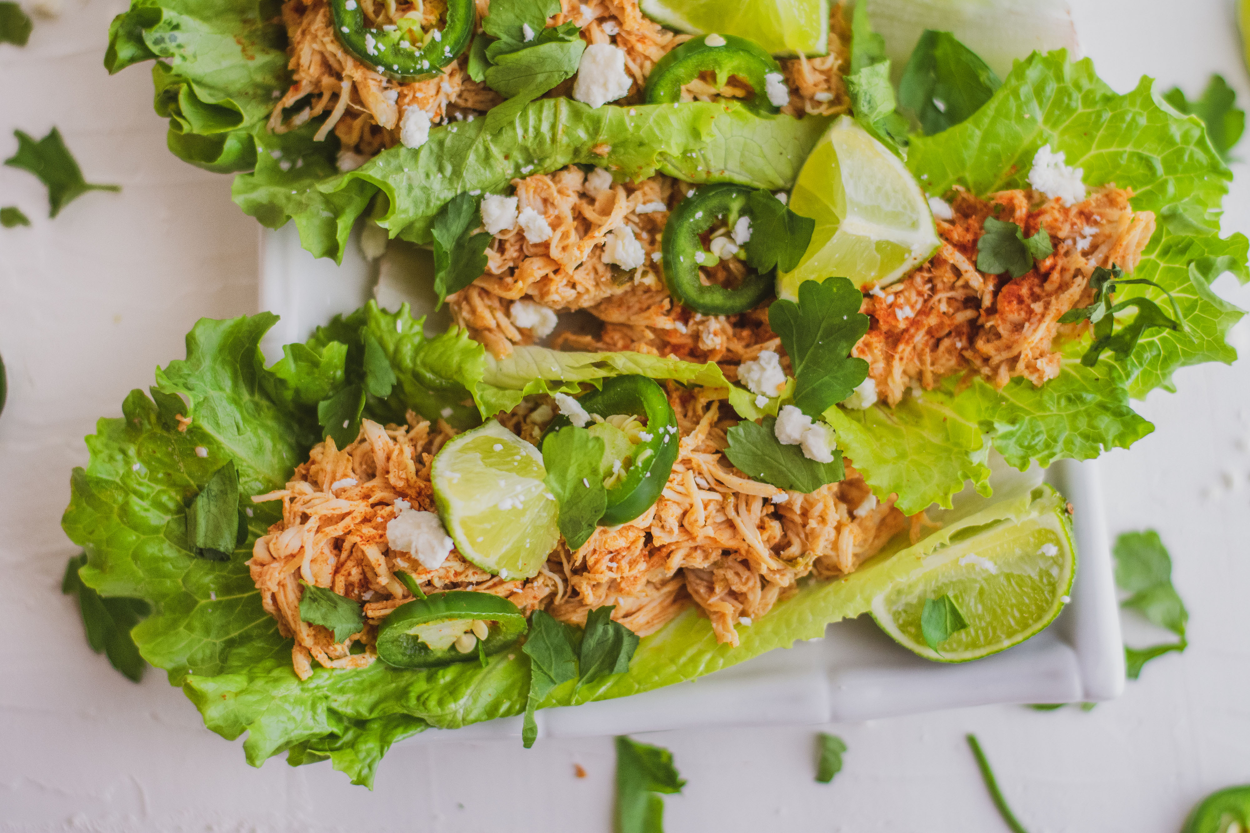 Shredded chicken tacos in lettuce wraps with fetta cheese, limes and jalapenos on top