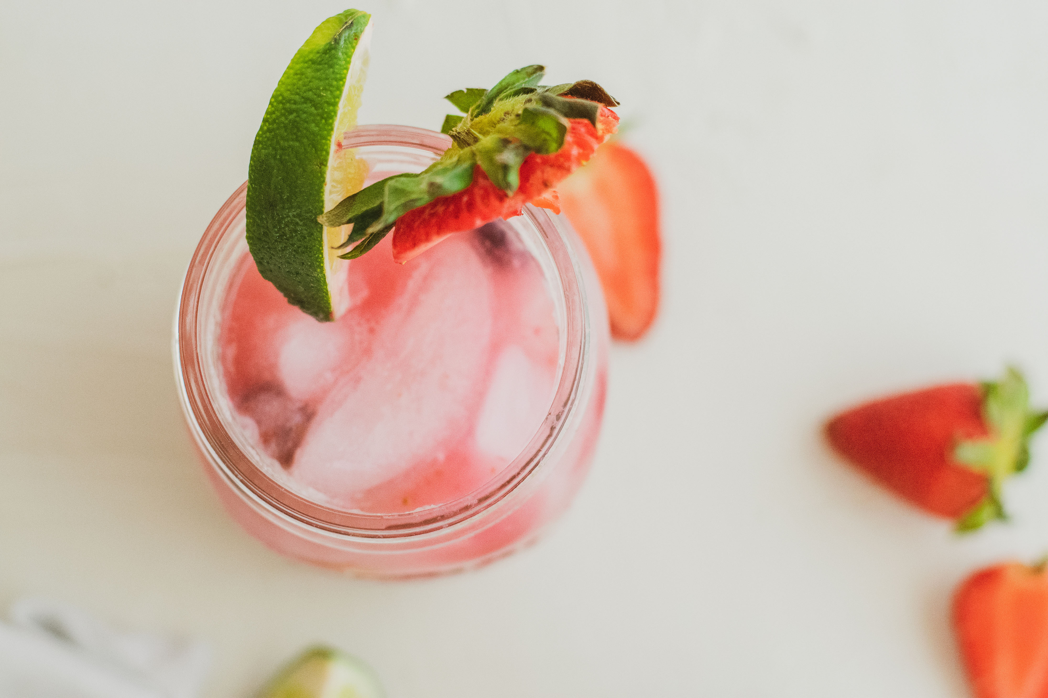 Frothy Pink Drink on a white surface with strawberries and lime slices on the surface and rim of glass