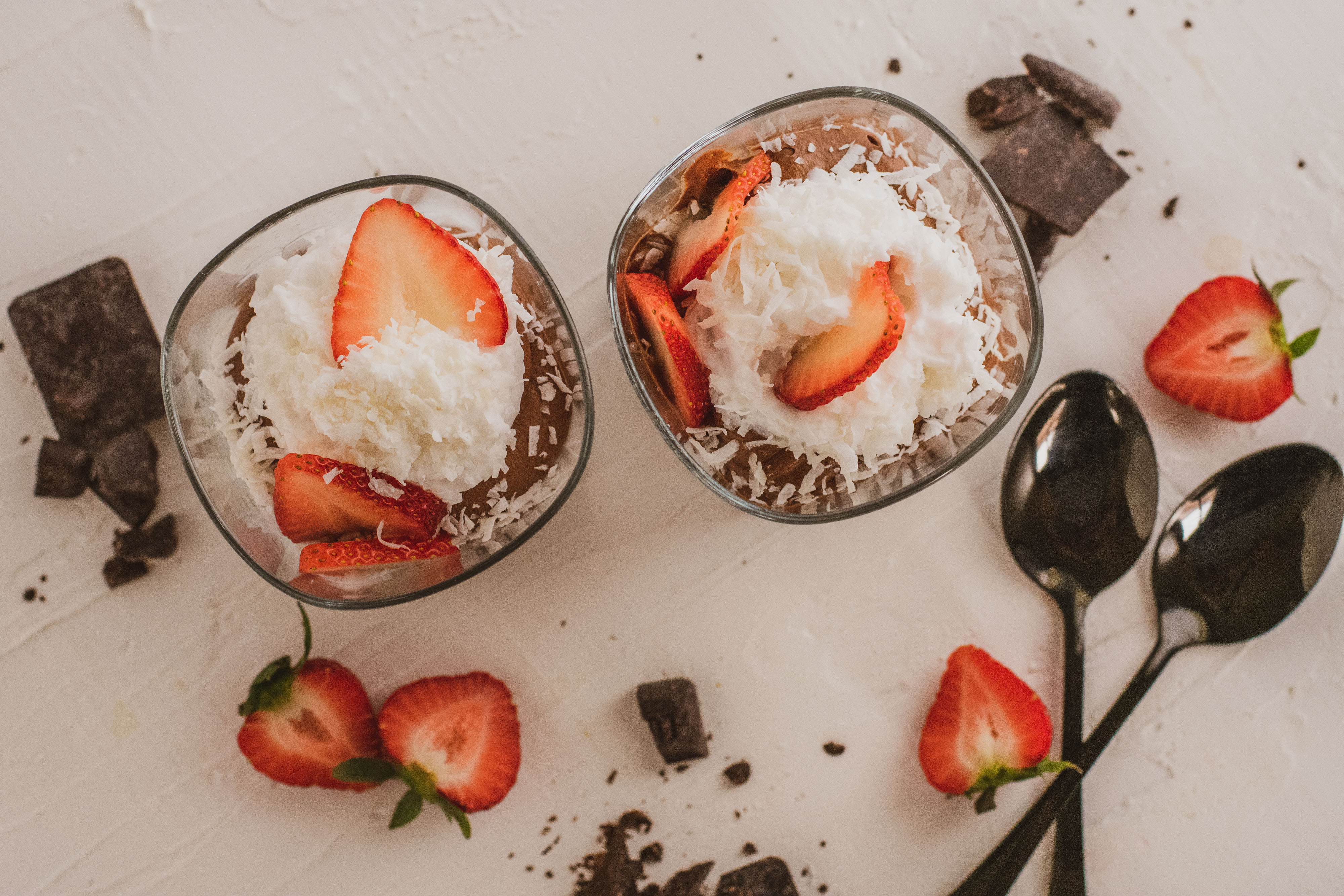 low carb Chocolate pudding with whipped cream topped with strawberries and two black spoons on a white surface
