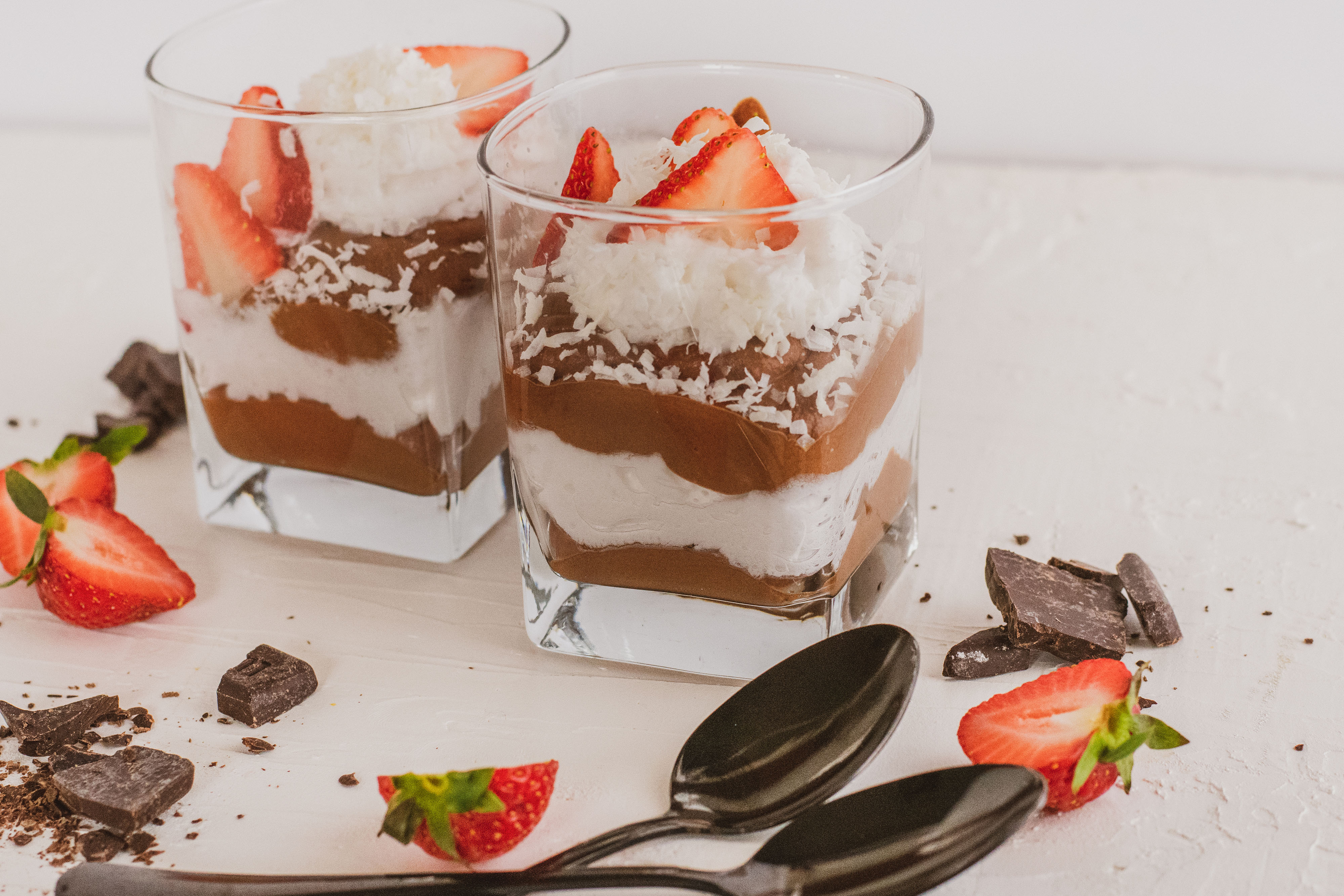low carb Chocolate pudding with whipped cream topped with strawberries and two black spoons on a white surface