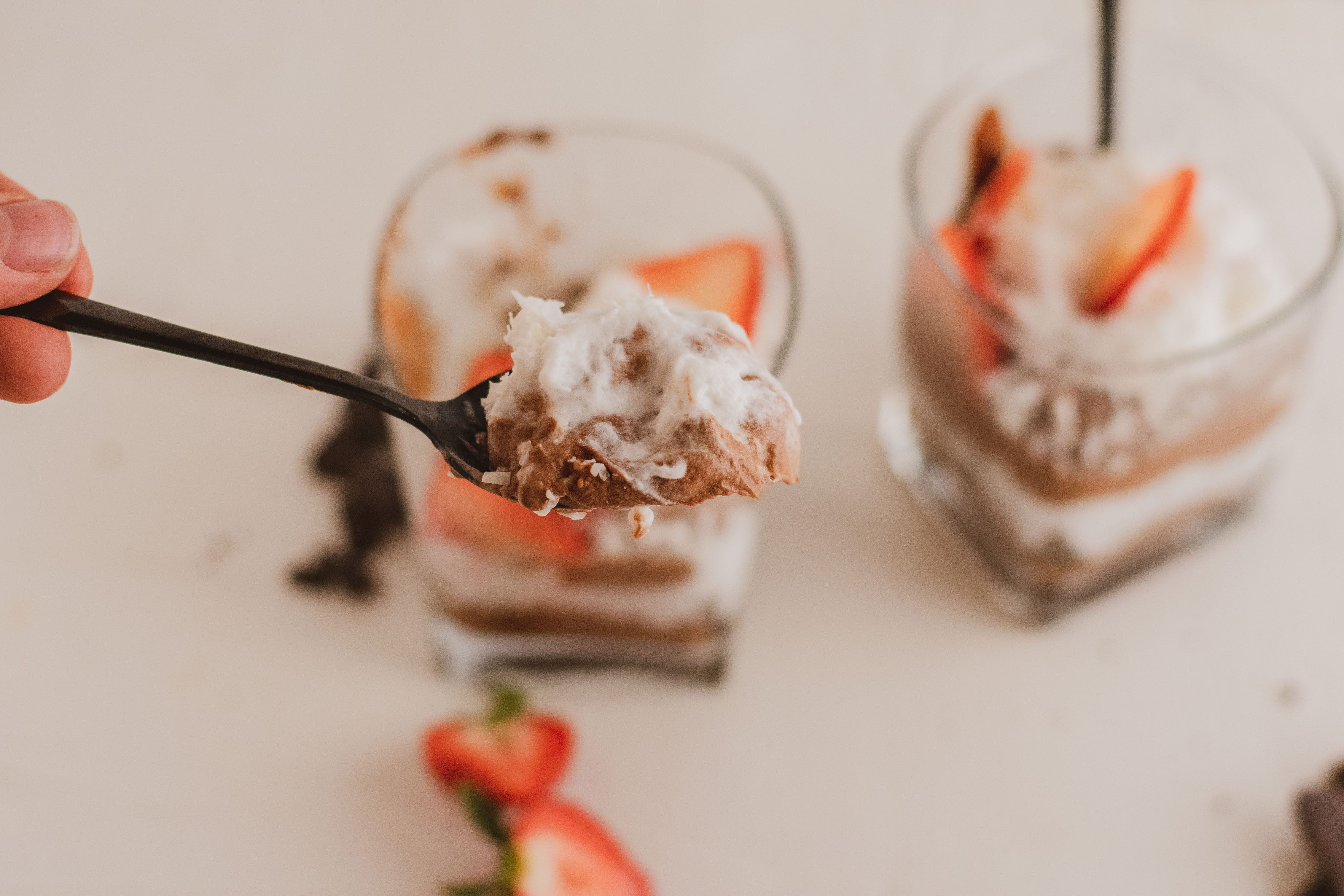 low carb Chocolate pudding with whipped cream topped with strawberries with a black spoon grabbing a bite on a white surface