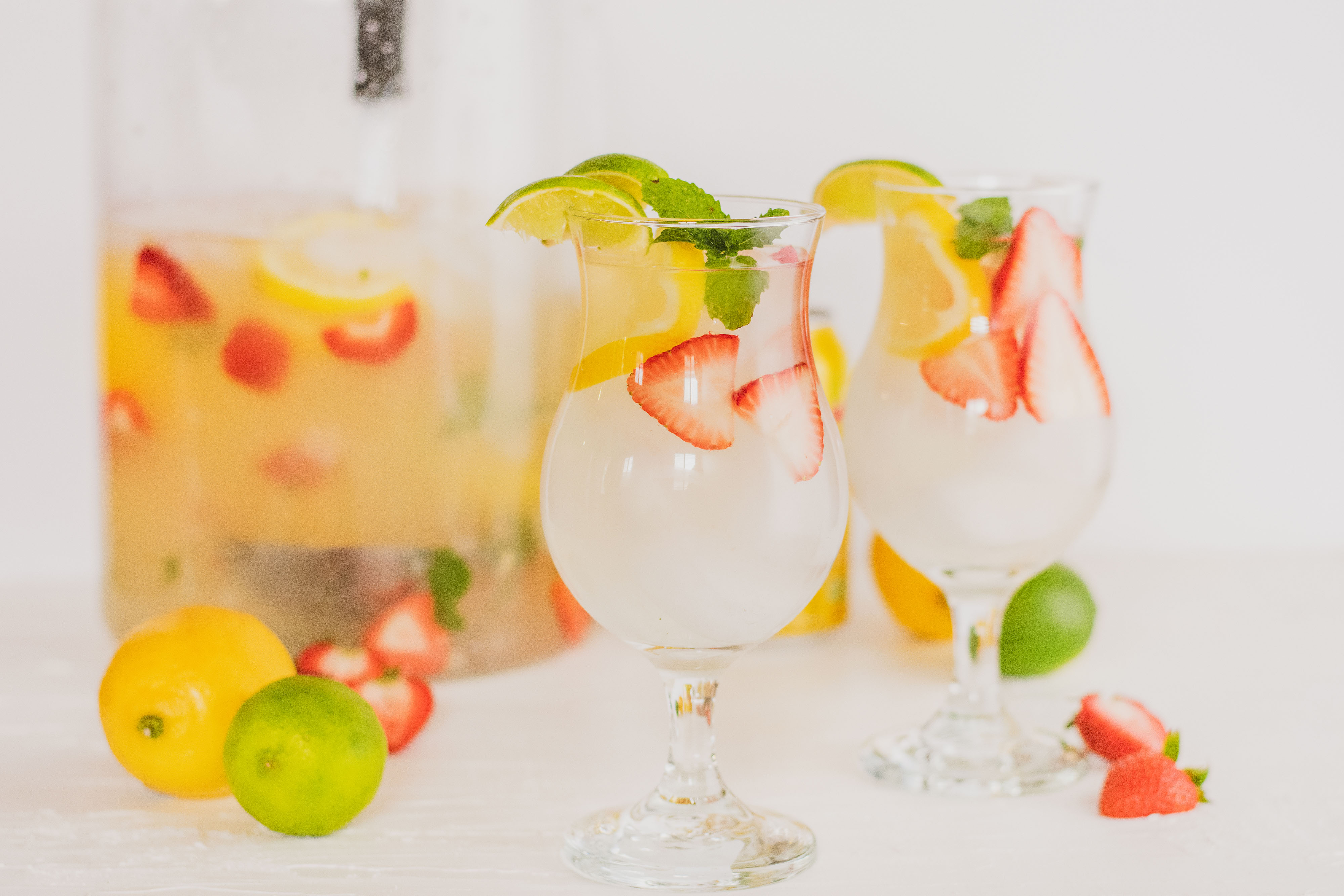 Two glasses with low carb strawberry lemonade mojito drink. With sliced strawberries and lemons and mint leaves on a white surface.