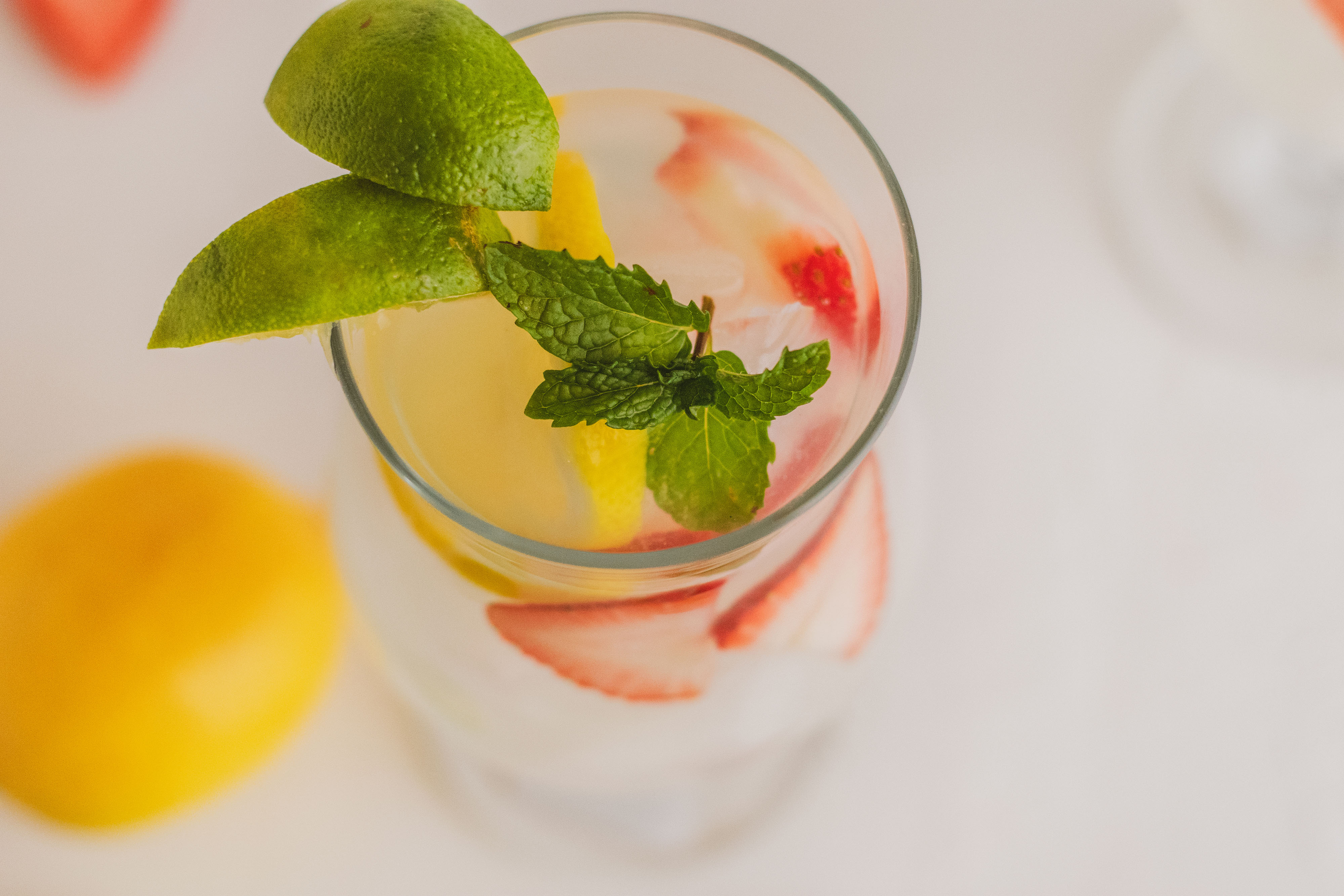 Two glasses with low carb strawberry lemonade mojito drink. With sliced strawberries and lemons and mint leaves on a white surface.