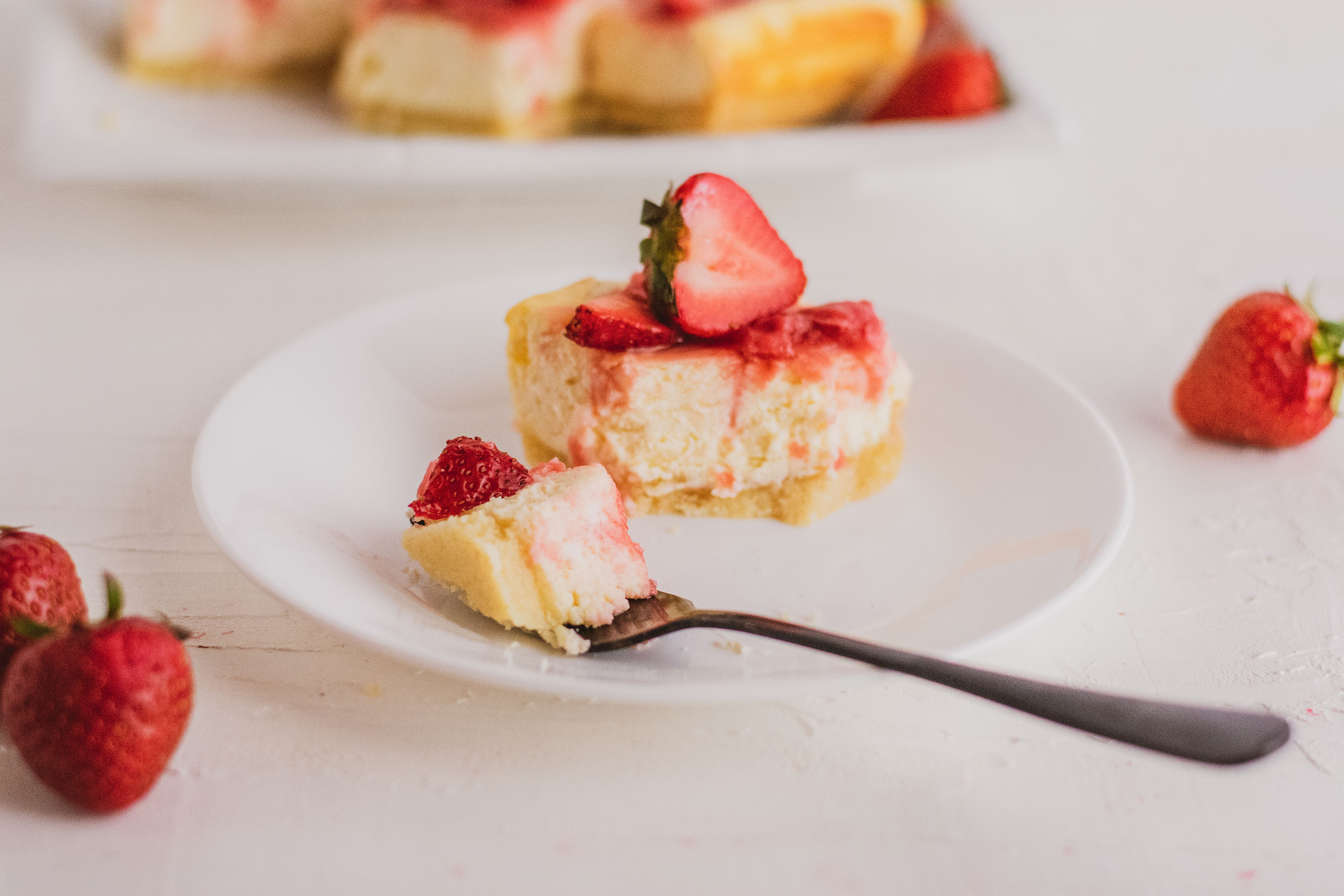 Low carb strawberry cheesecake with a strawberry jam on top on a white surface with strawberries on the sides. 