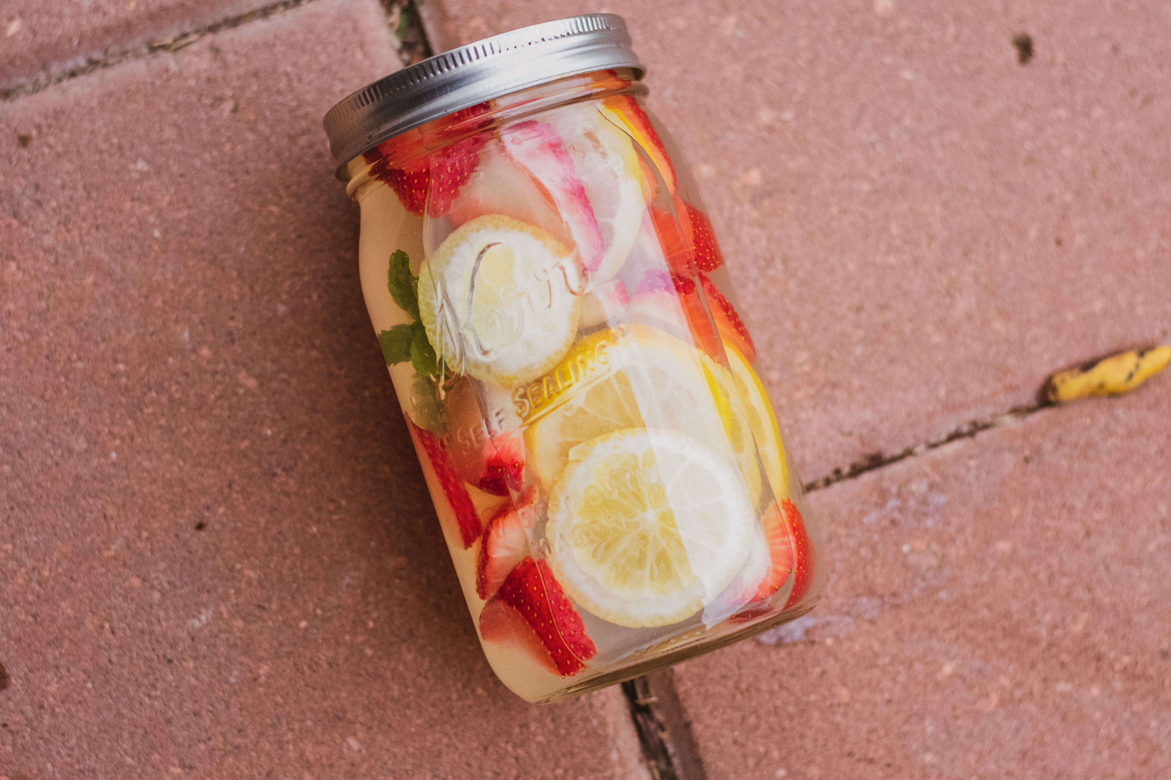 A mason jar with low carb strawberry lemonade mojito drink. With sliced strawberries and lemons and mint leaves on a brick.