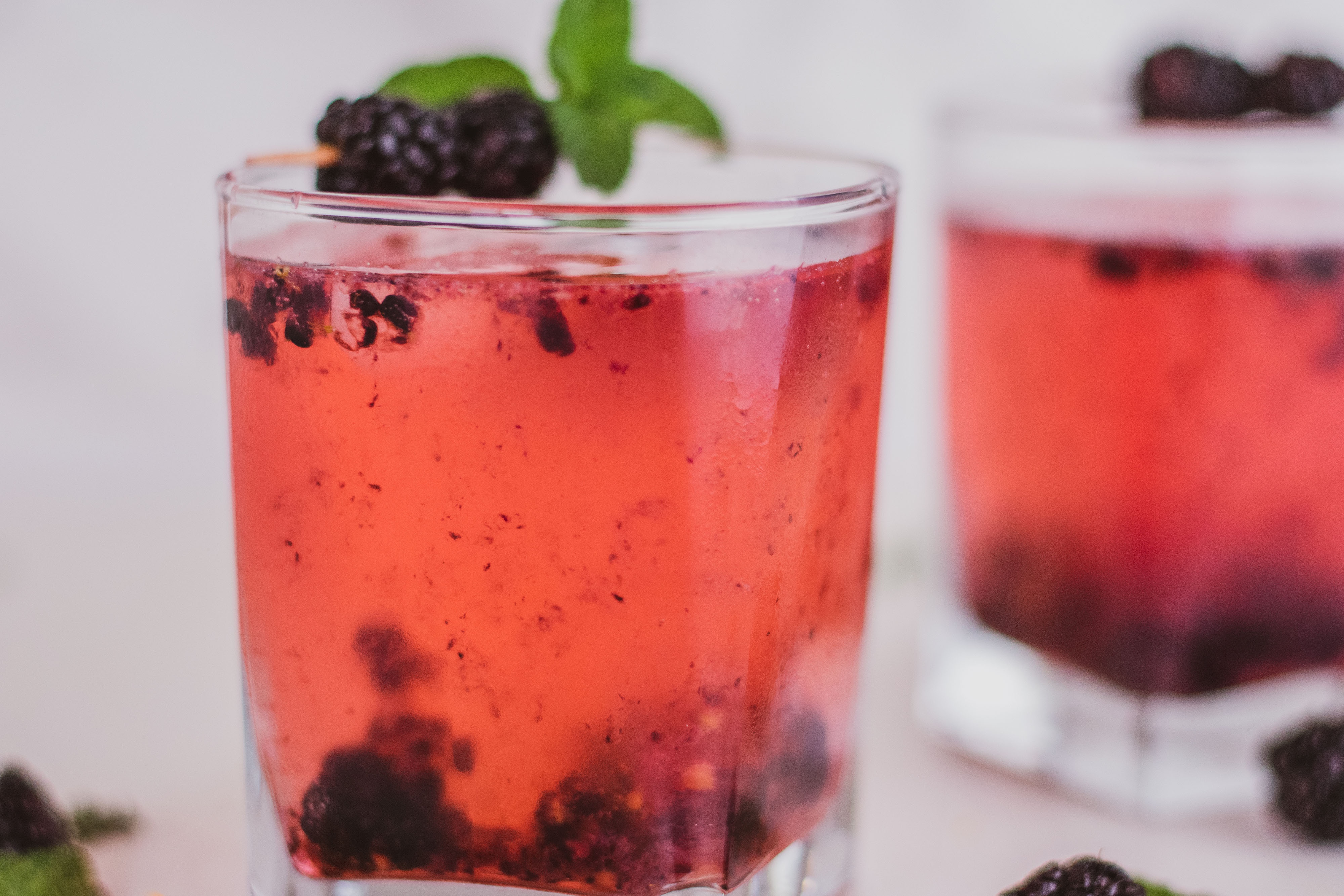 Keto blackberry rum cocktail in a short glass with blackberries on top on a white surface.