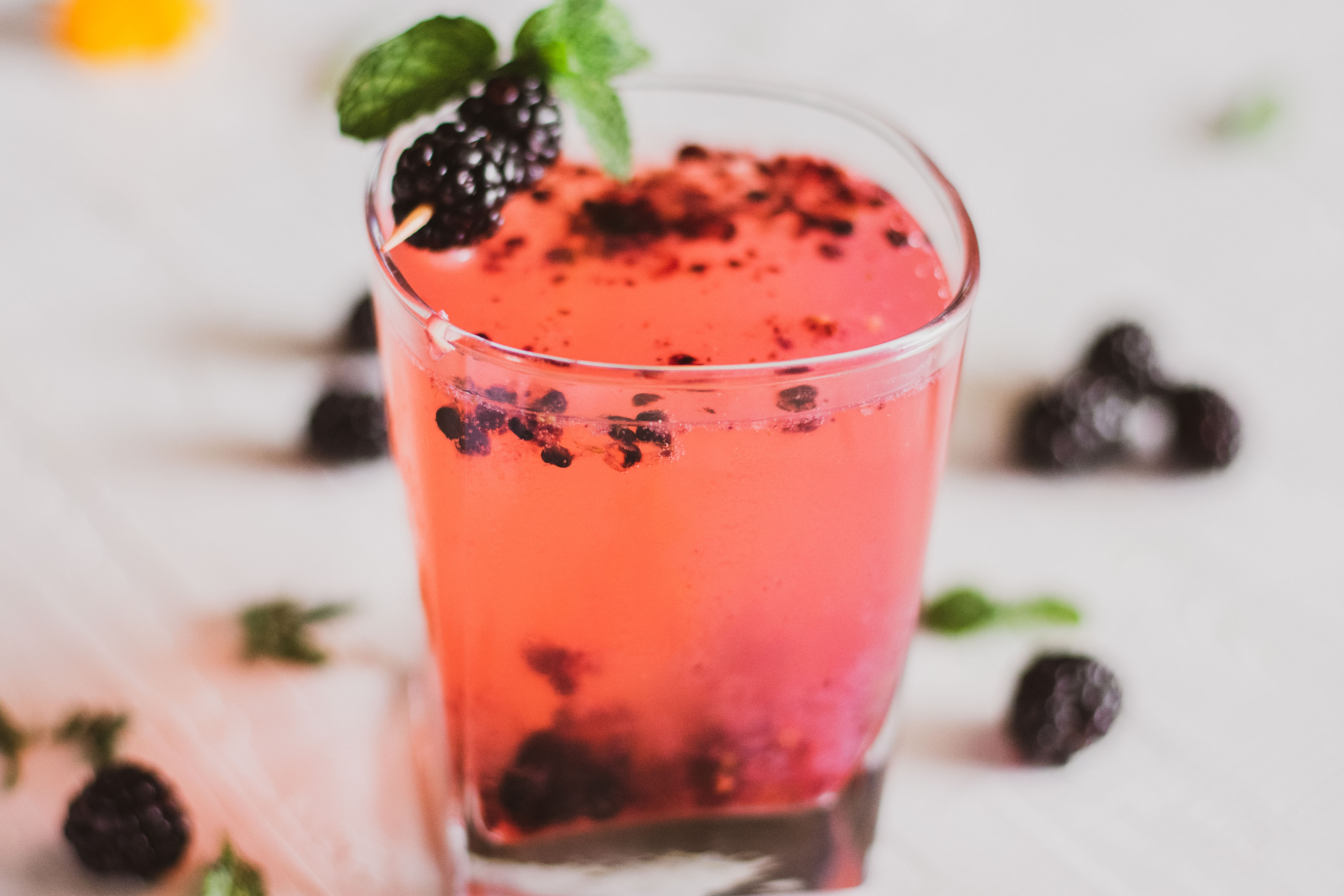 Keto blackberry rum cocktail in a short glass with blackberries on top on a white surface.
