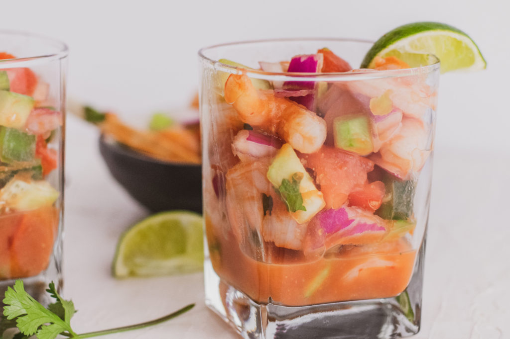 Keto ceviche in a glass cup with a lime on the side on a white surface.