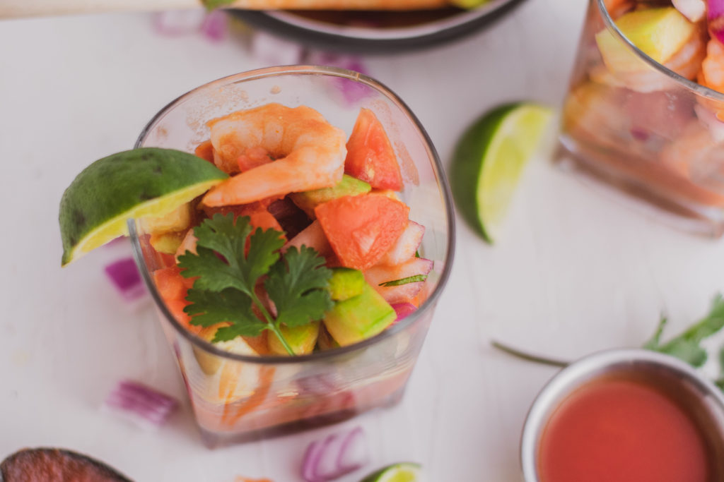 Keto ceviche in a glass cup with a lime on the side on a white surface.