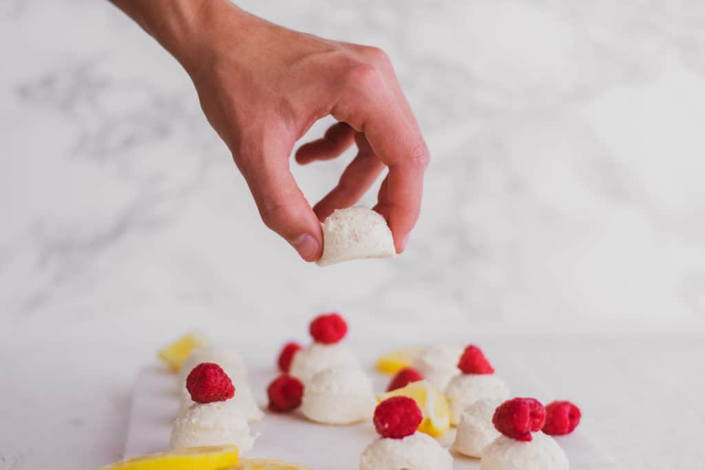 Keto creamy lemon fat bombs with raspberries on a white surface with a hand picking one up