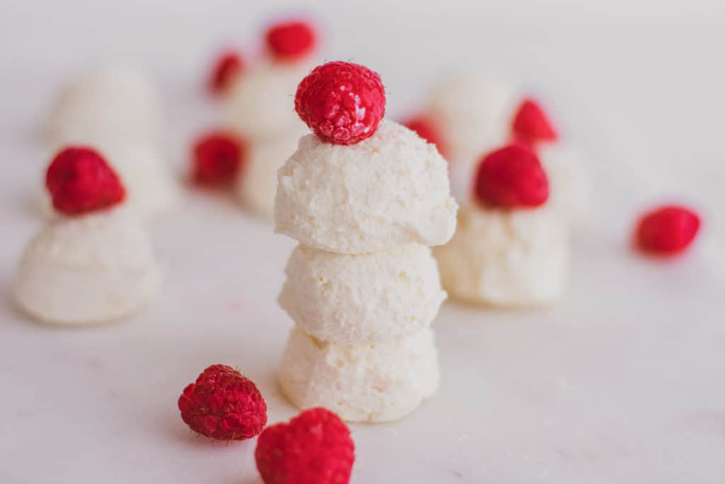 Keto creamy lemon fat bombs with raspberries on a white surface