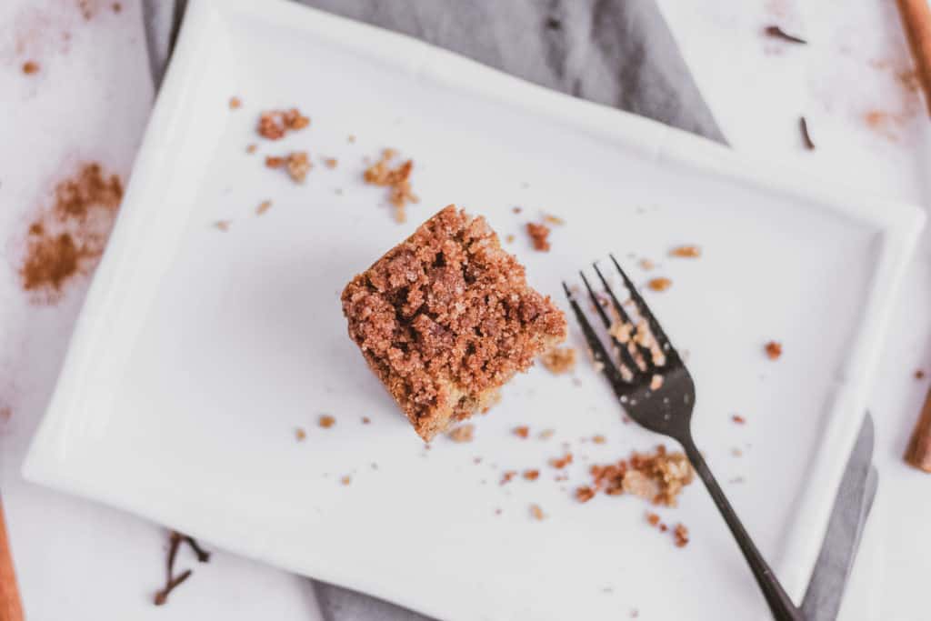 Keto apple spice cake slice on a white plate with a fork on the side on a grey napkin and white surface.