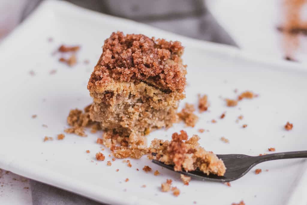 Keto apple spice cake slice with a fork taking a bite on a grey napkin and white surface.