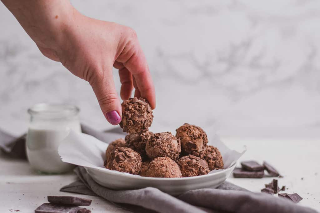 Keto peanut butter brownie fat bombs with a hand holding it over a bowl of the recipe.