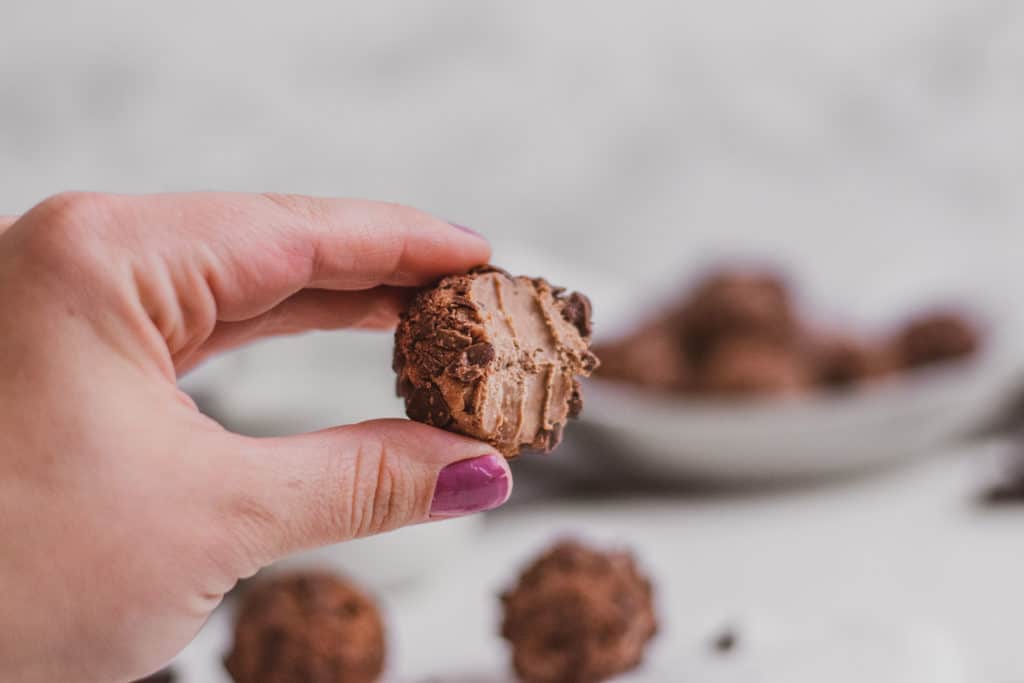 Keto peanut butter brownie fat bombs with a bite taken out with a hand holding it.