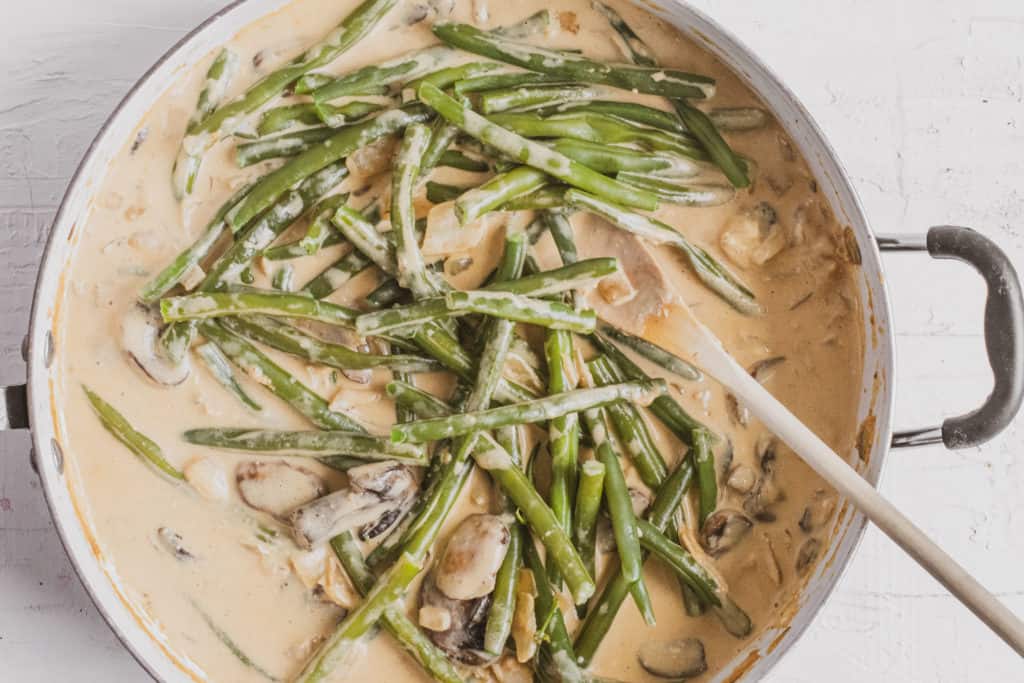 Green beans in creamy mushroom and onion sauce in a white skillet for the second step of the recipe.