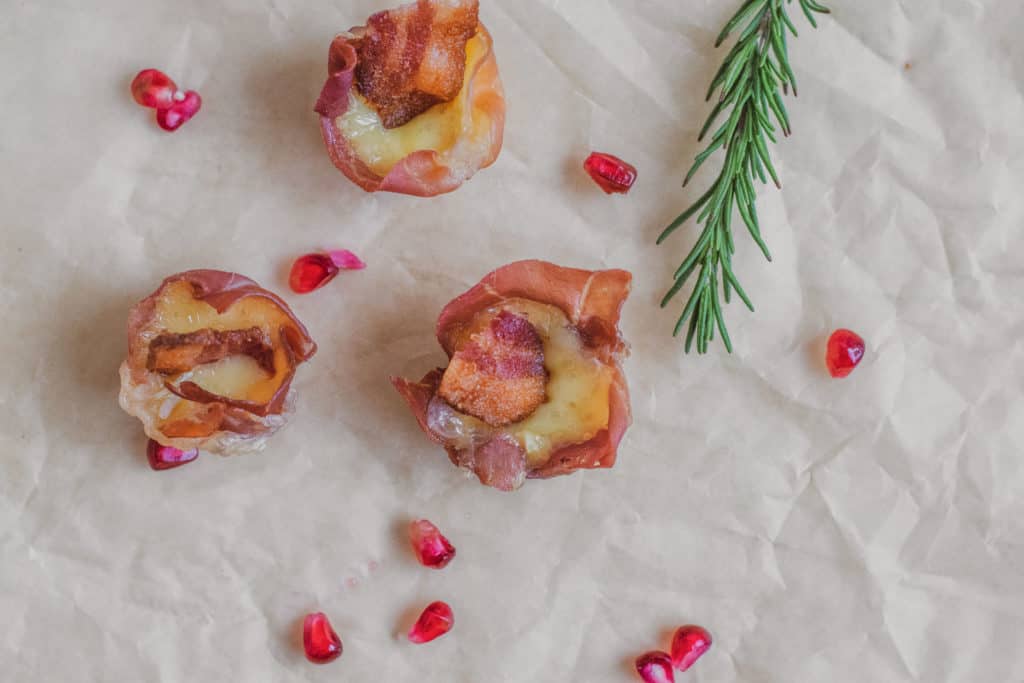 Prosciutto Brie Cups with a rosemary, and pomegranate in the background.