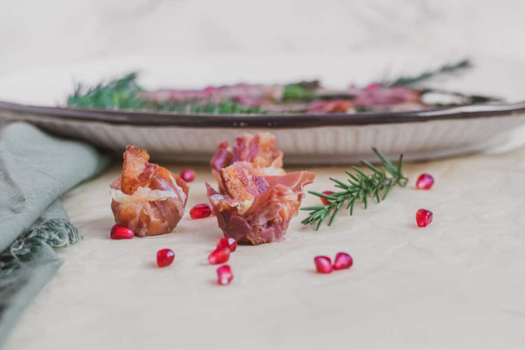 Prosciutto Brie Cups with a plate, green napkin, rosemary, and pomegranate in the background.