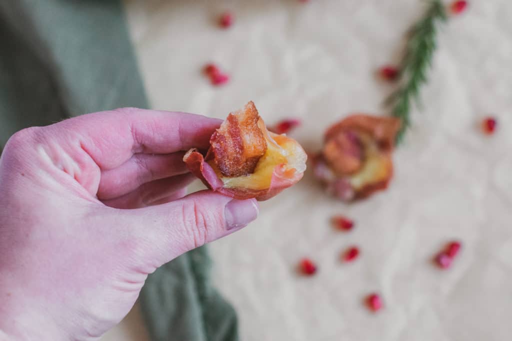 Prosciutto Brie Cups in a hand with a green napkin, rosemary, and pomegranate in the background.