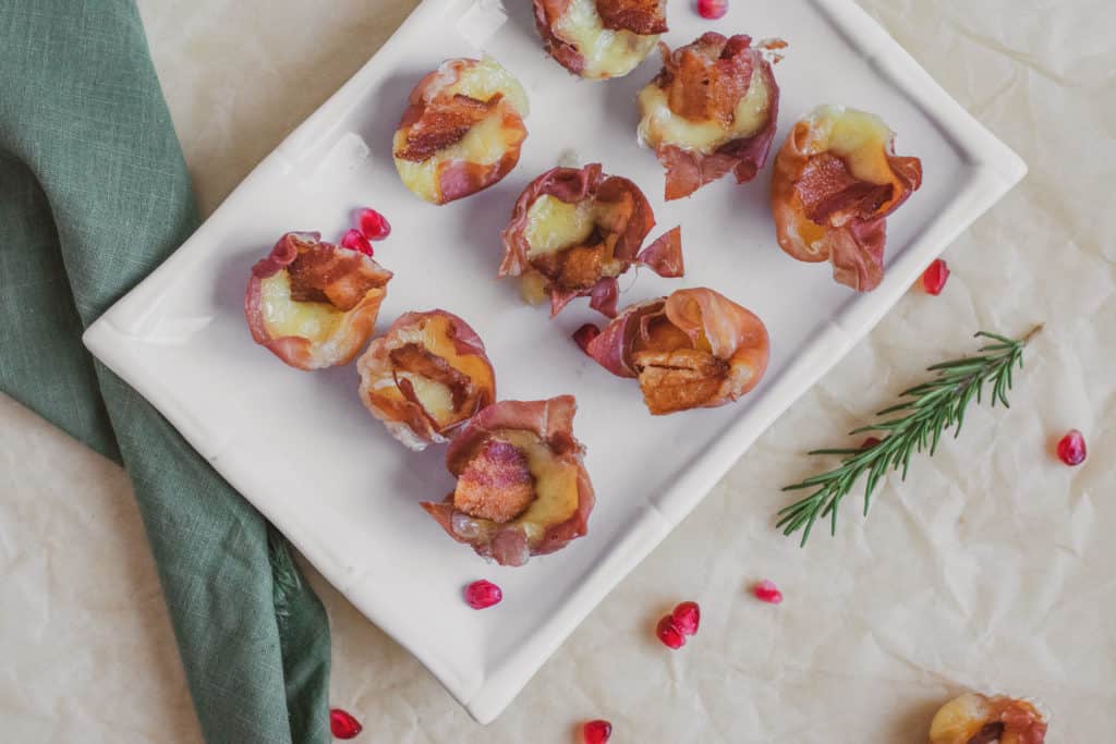 Prosciutto Brie Cups with a plate, green napkin, rosemary, and pomegranate in the background.