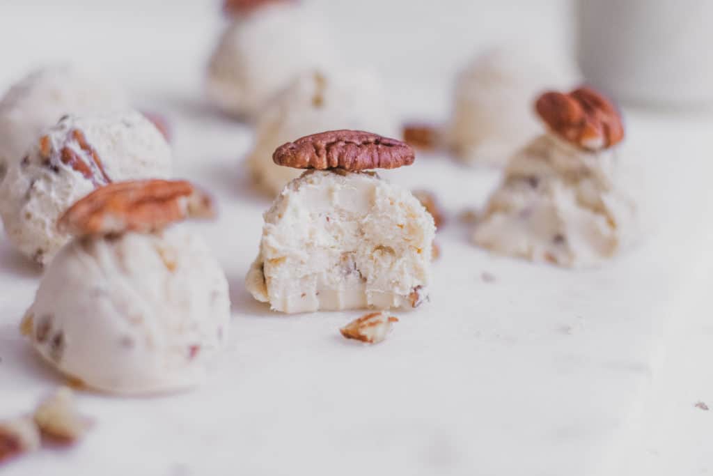 Keto butter pecan fat bombs with pecans on top and on a white surface.
