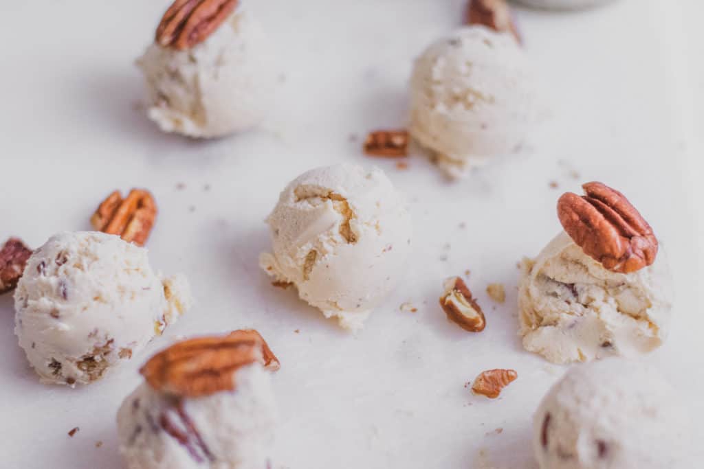 Keto butter pecan fat bombs with pecans on top and on a white surface.