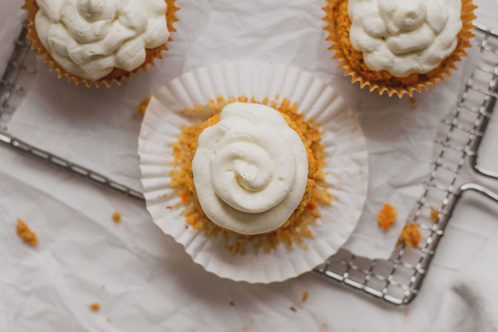 Keto carrot cake muffins with cream cheese frosting on a white surface and wire wrack.
