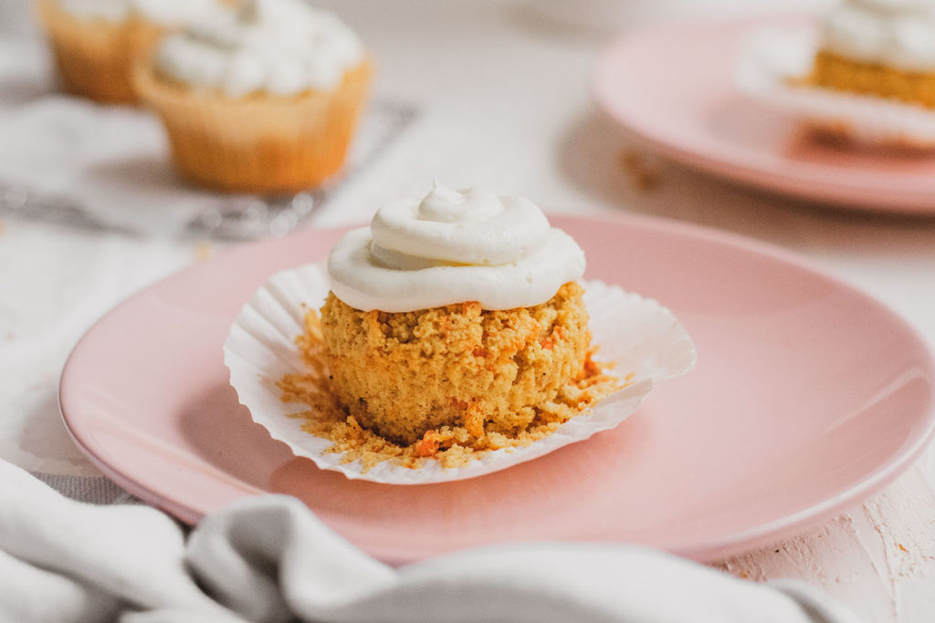 Keto carrot cake muffins with cream cheese frosting on pink plates on a white surface. 