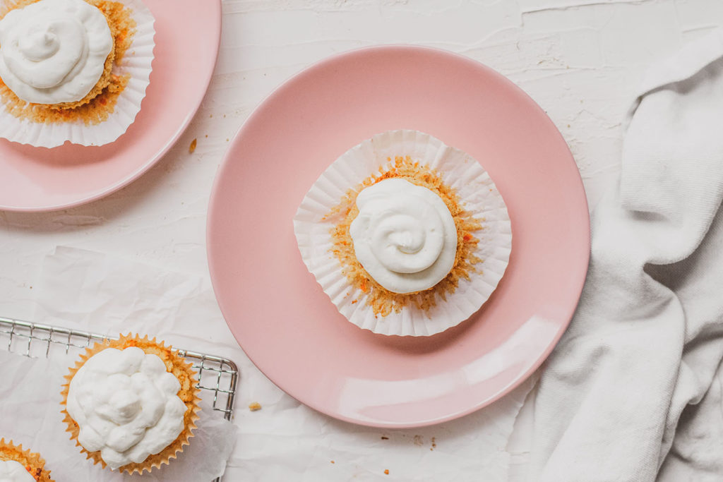 Keto carrot cake muffins with cream cheese frosting on pink plates on a white surface. 