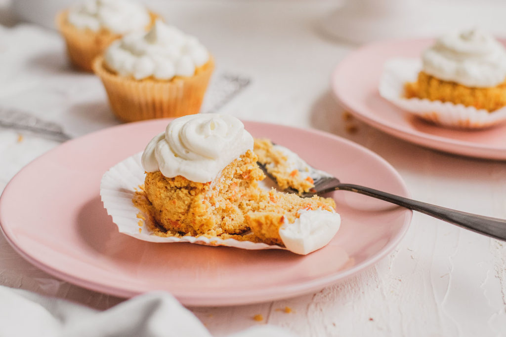 Keto carrot cake muffins with cream cheese frosting with a black fork taking a bite on pink plates. 