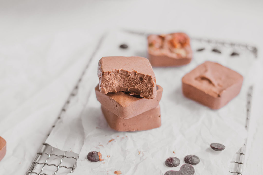 Dairy Free Chocolate Peanut Butter Fat Bombs stacked with a bite taken out on a white surface.