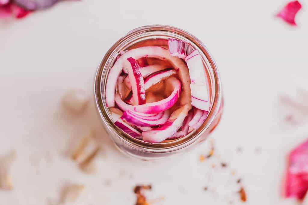 Low carb Pickled Red Onions in a mason jar on a white surface.
