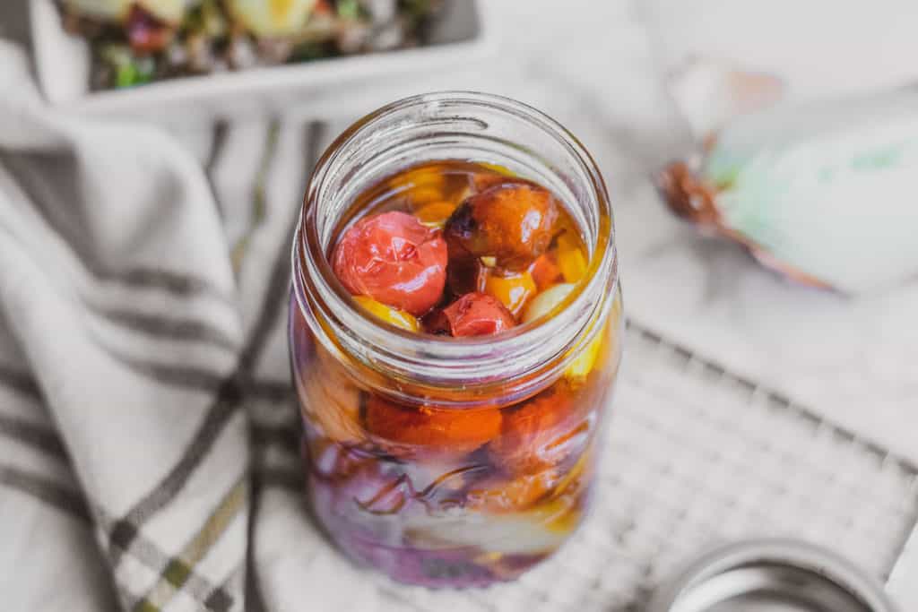 Keto cherry tomato confit in a jar on a white surface with a napkin on the side.